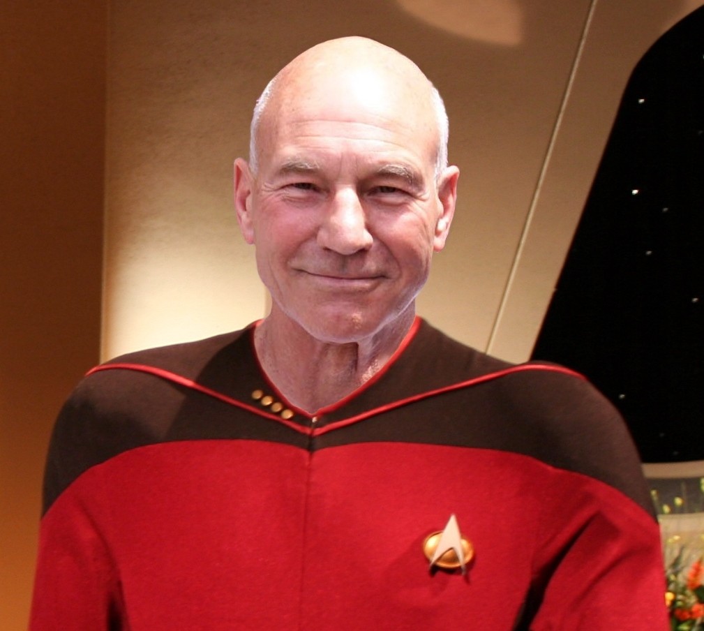 Portrait image of Jean Luc-Picard in a red Star Trek The Next Generation Uniform, with his captains quarters in the background