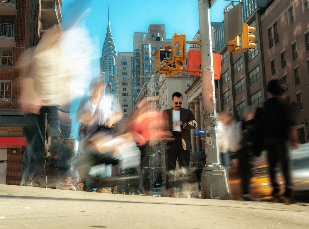A woman with wavy hair smiles while holding a microphone, speaking into the audience against a colorful backdrop.