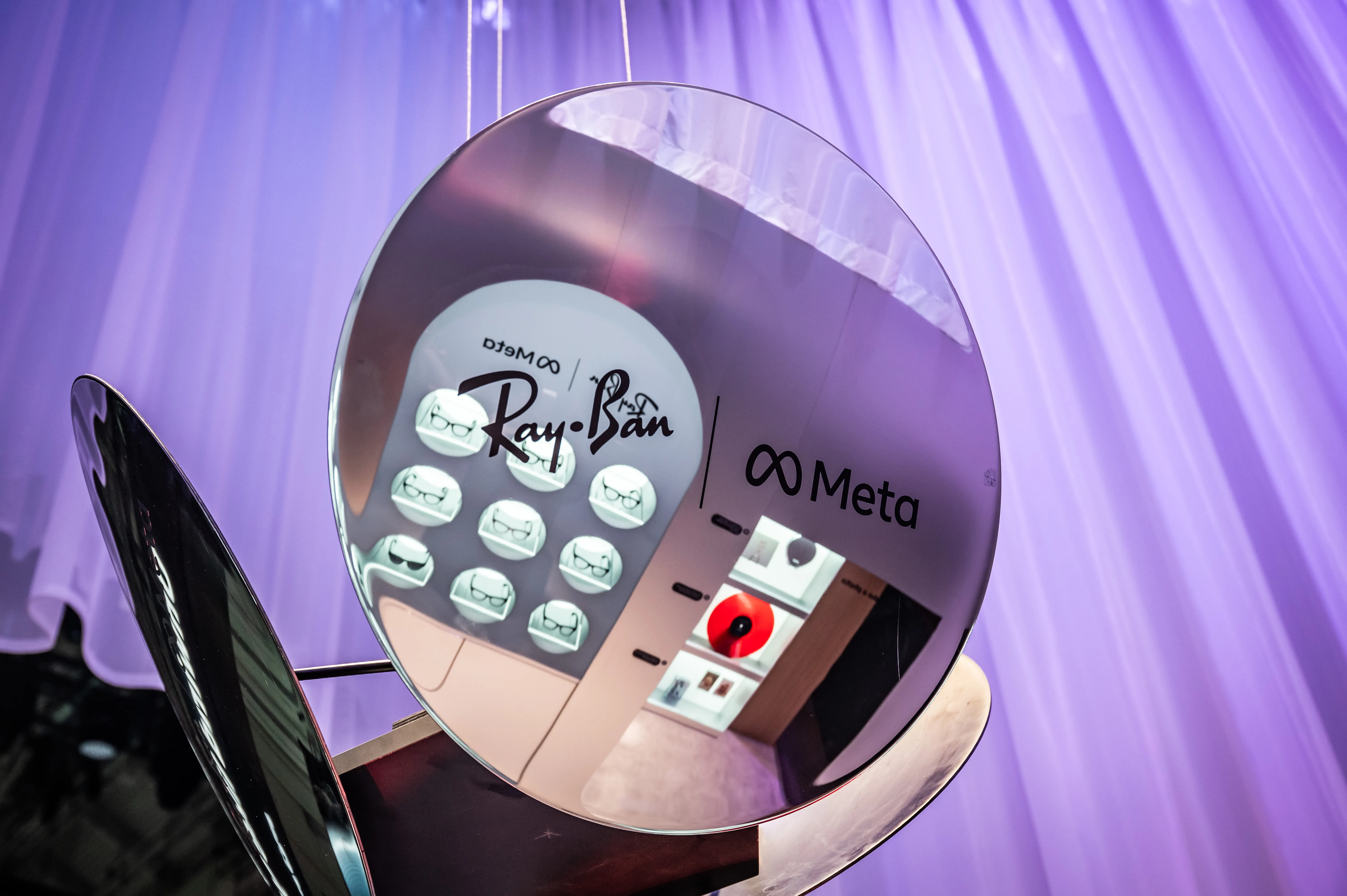 Round mirror reflecting the Ray-Ban Meta product wall, framed by purple-lit curtains.