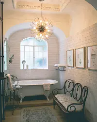 Elegant bathroom with freestanding bathtub, arched window, chandelier, and neutral finishes