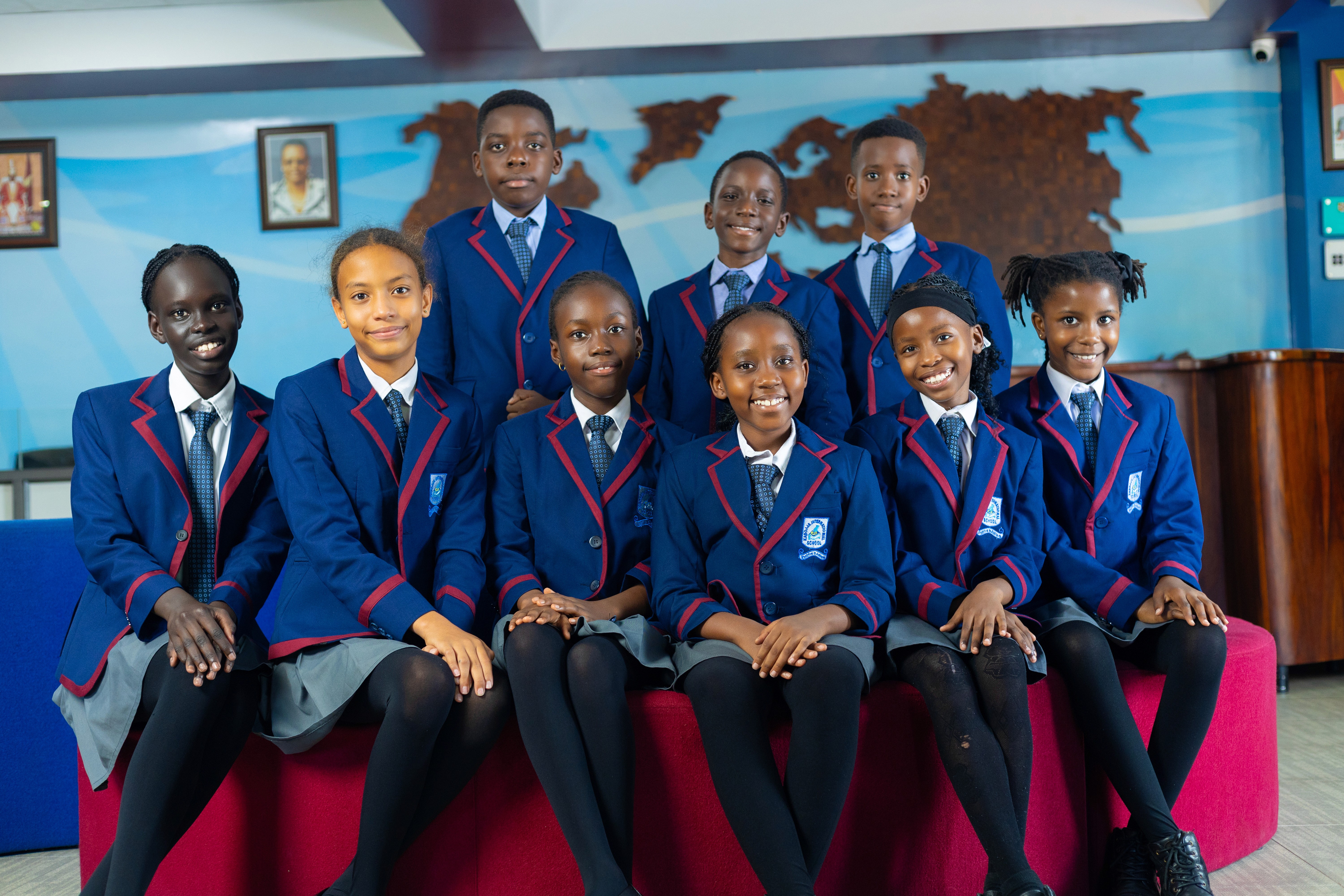 A student wearing a red uniform sits while holding a book in his hands