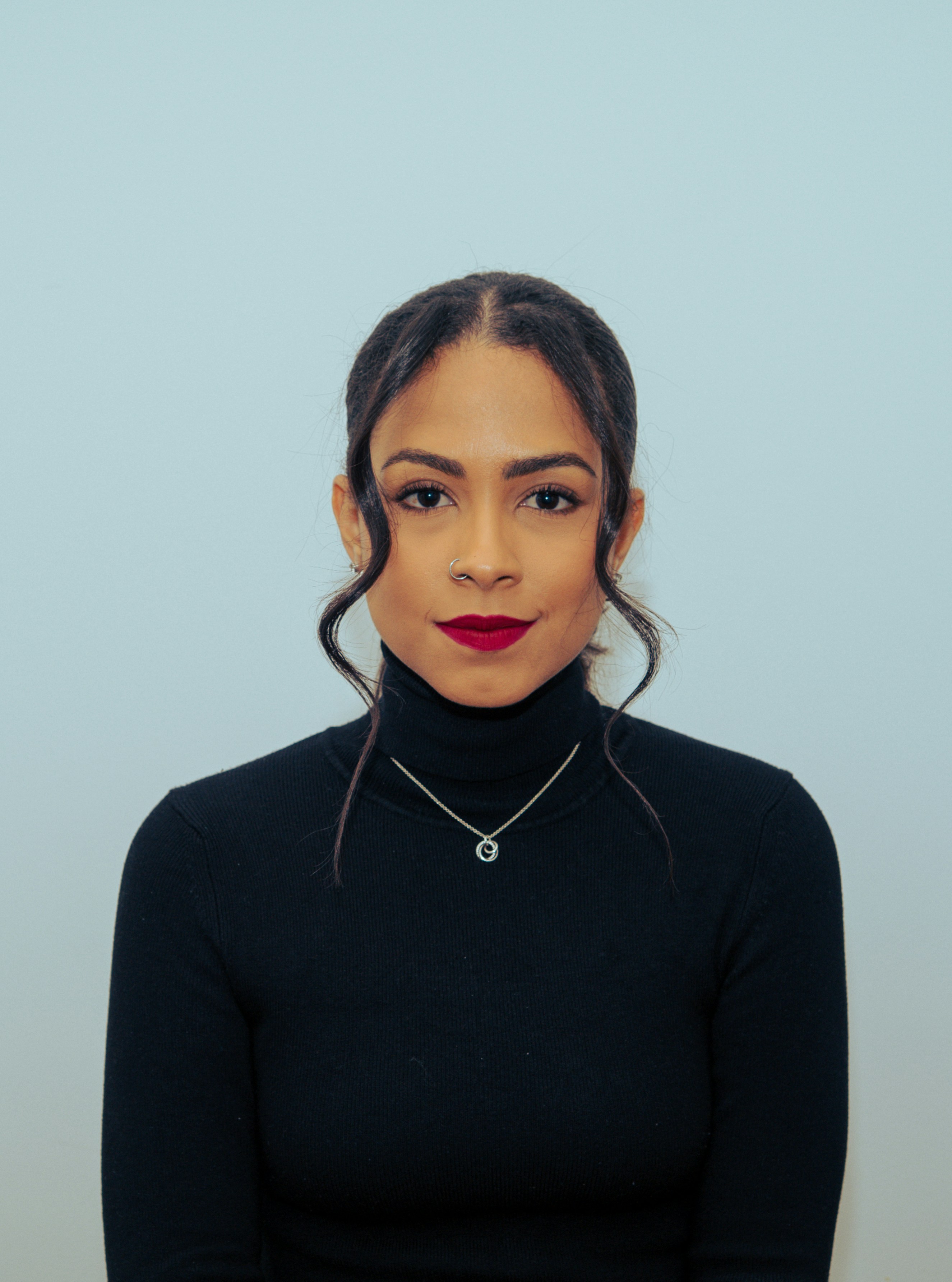Woman with dark hair wearing a black turtleneck and necklace.
