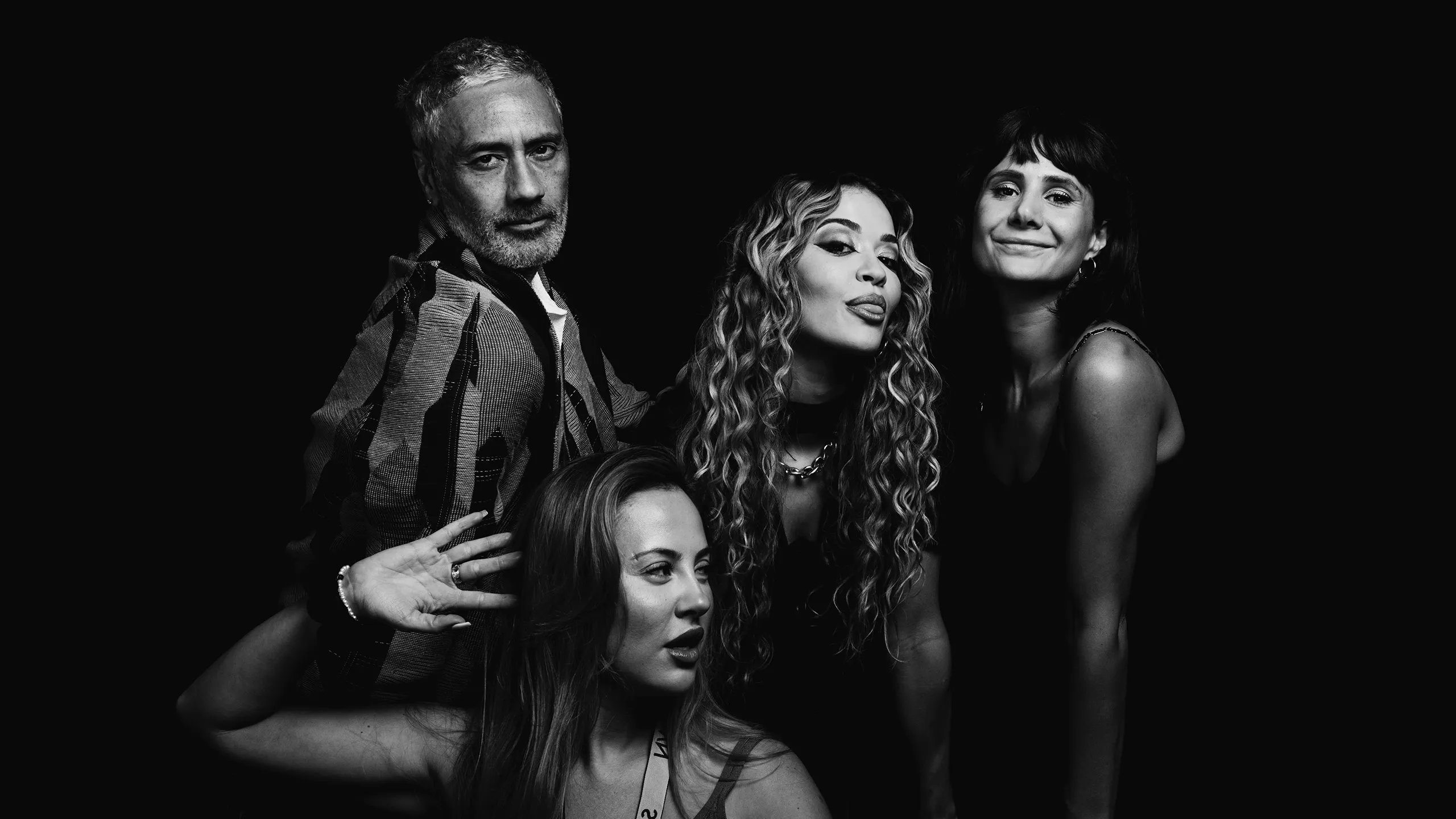 Black and white group portrait featuring Rita Ora and Taika Waititi in a candid moment.