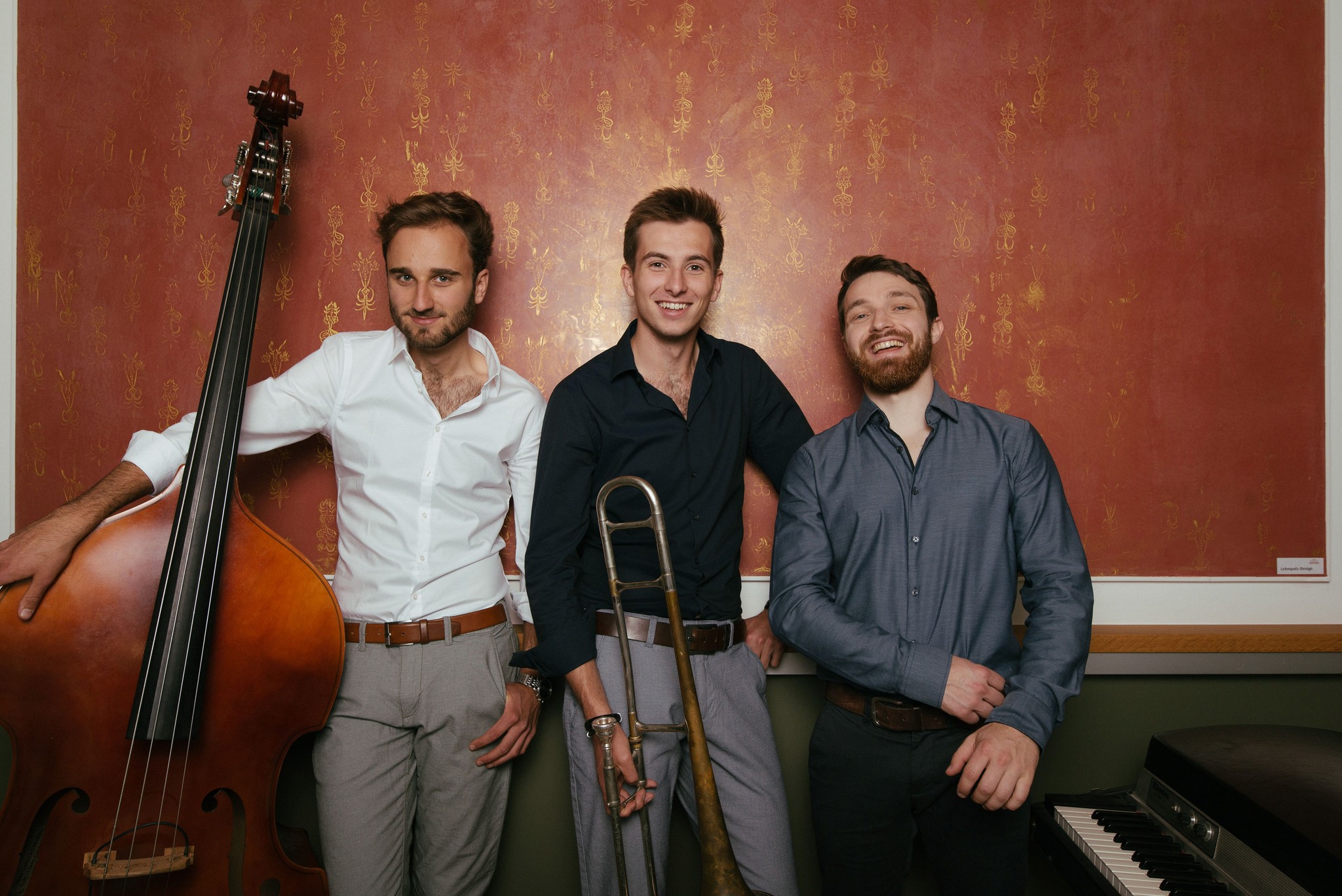 Musiker der Hop Jazz Group mit Kontrabass und Posaune vor einer gold-roten Wand.