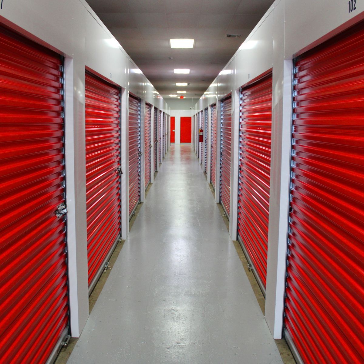 Storage units with red doors, creating a long perspective down the hallway towards a single red door.