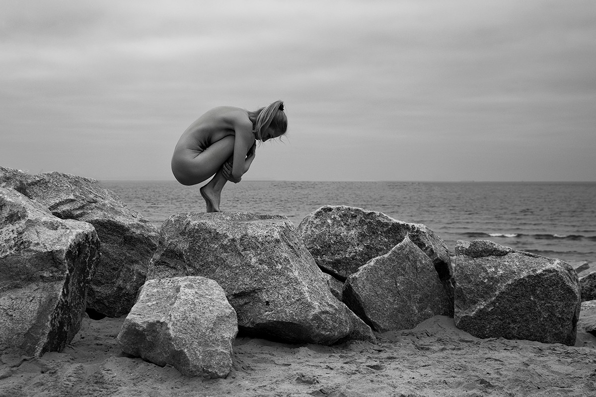 Woman crouching on a rock by the sea, February, Baltic Sea - Stone and Skin - Agnieszka Czyzkowska Photography