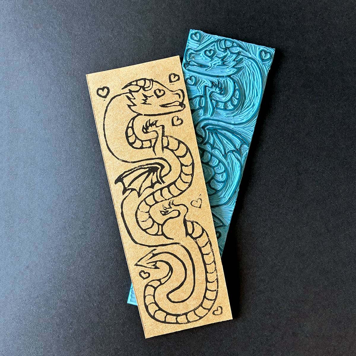 Linogravure d'un marque page représentant un dragon avec un cœur à la place de l'œil