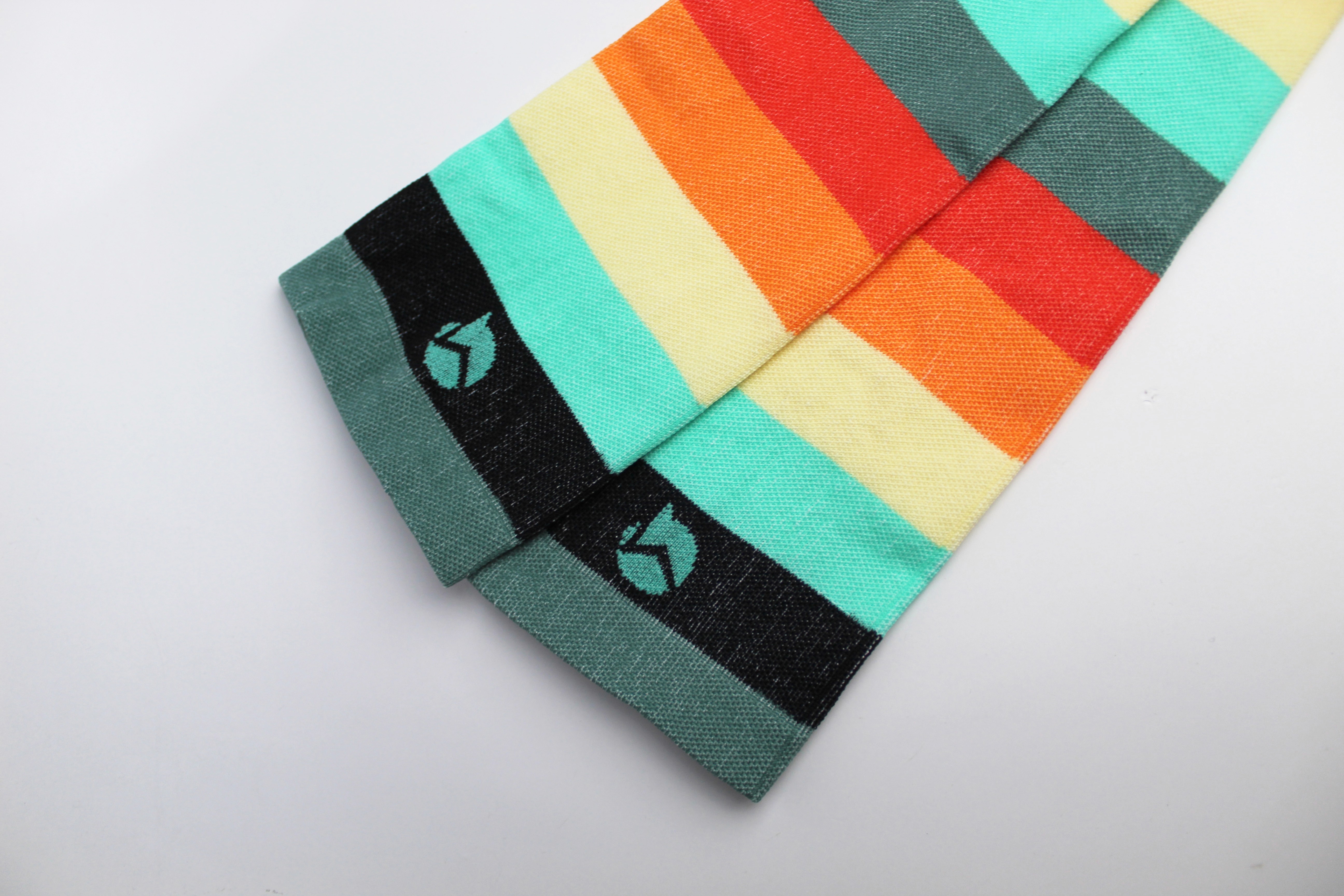 Two socks on a white backdrop showing the cuff and decoration up close. The sock is striped and is very colorful with a small logo on the second strip down from the cuff.