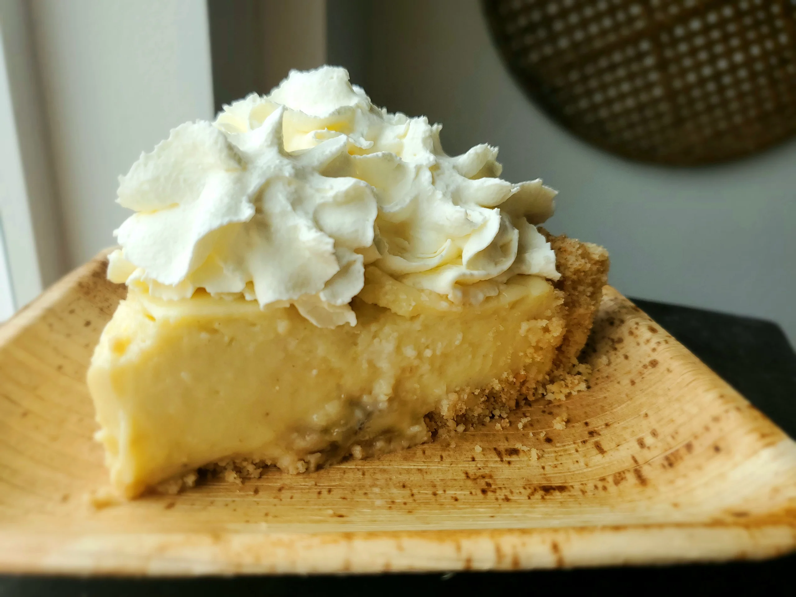 A thick slice of banana cream pie featuring a pale yellow custard layer, fresh banana slices, and a high peak of white whipped cream on a buttery cookie crust.
