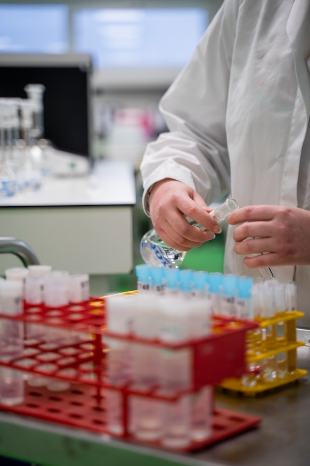 Scientist in a white coat handling test tubes in racks inside a laboratory.
