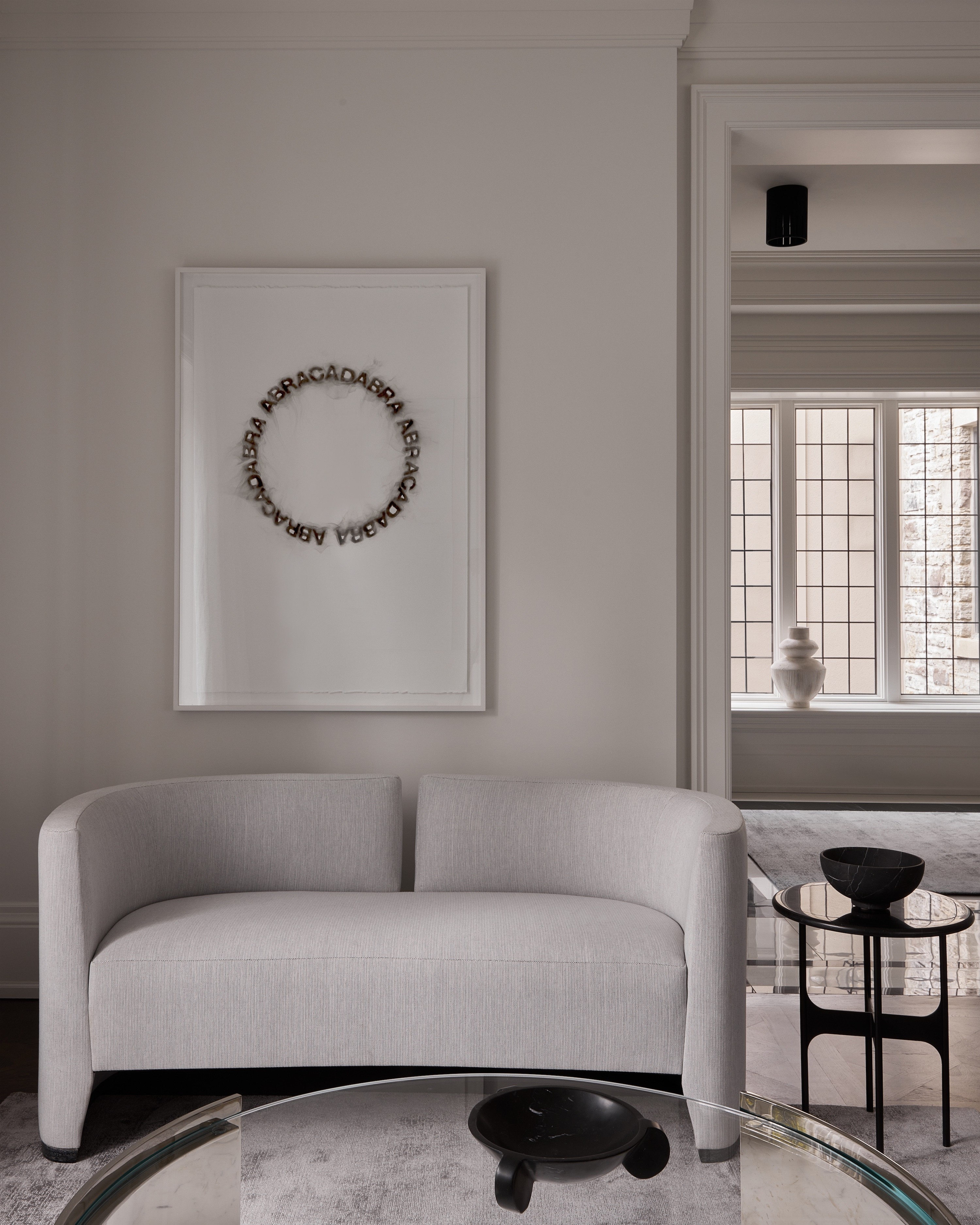 A pale sofa beneath a circular artwork, beside leaded windows