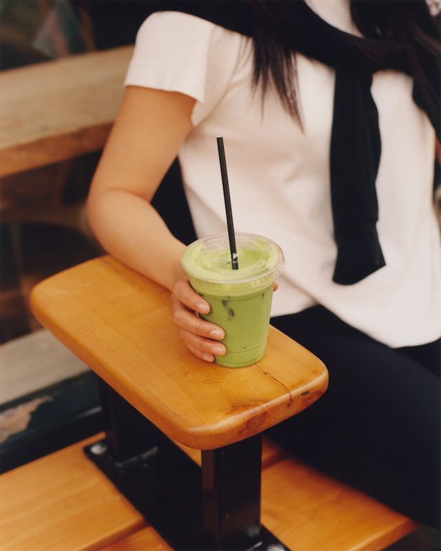 A person holding a green cup outside a NKORA Coffee Shop