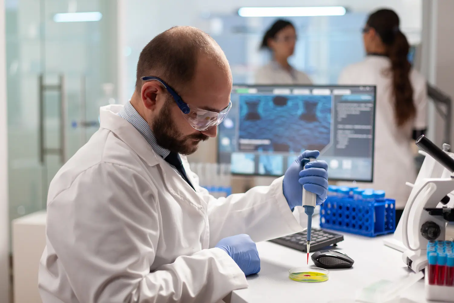 Scientifique en blouse et lunettes de protection déposant un échantillon à la pipette dans une boîte de Petri.