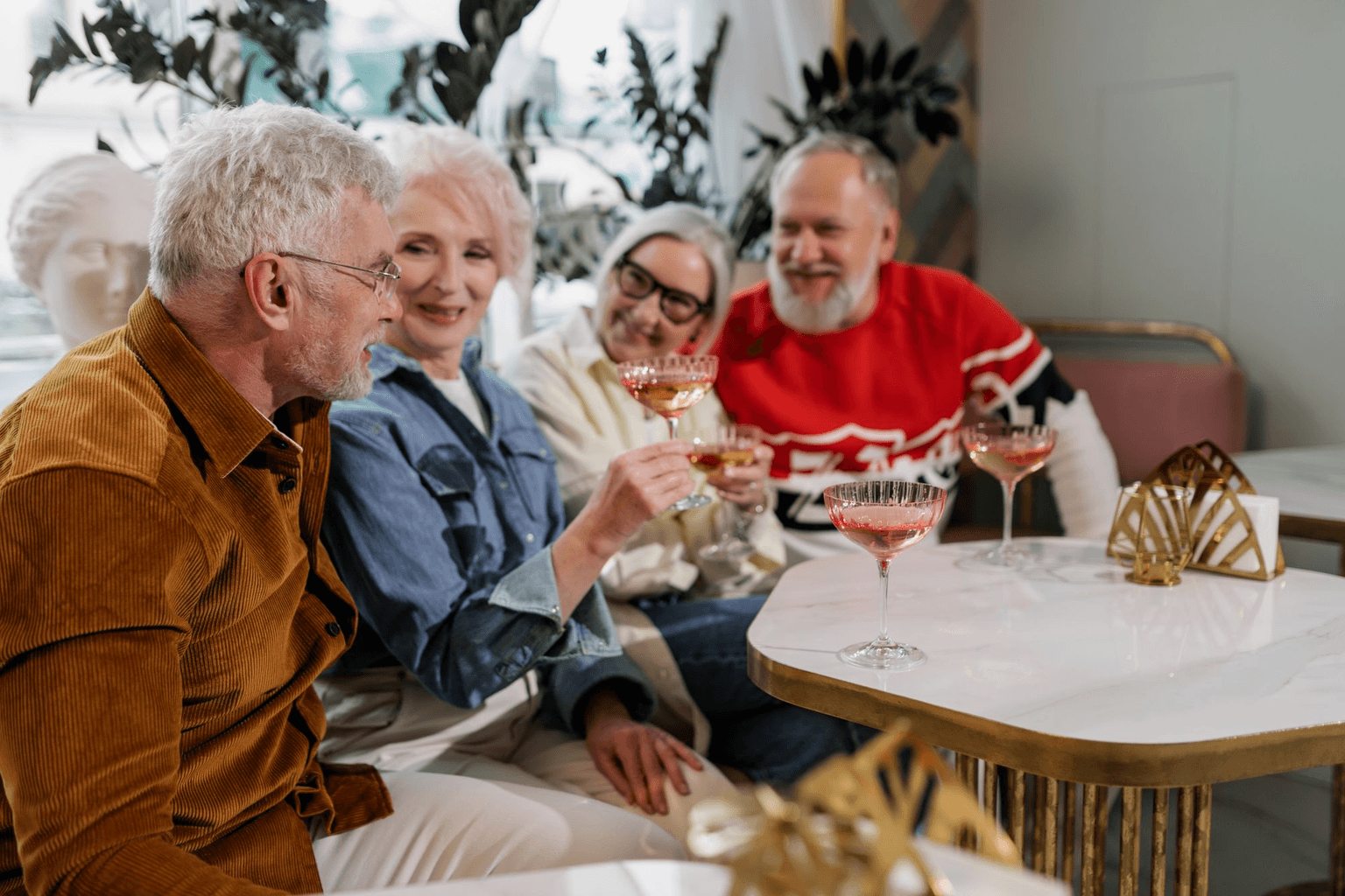 Four older friends raising their glasses together around a low table, laughing.