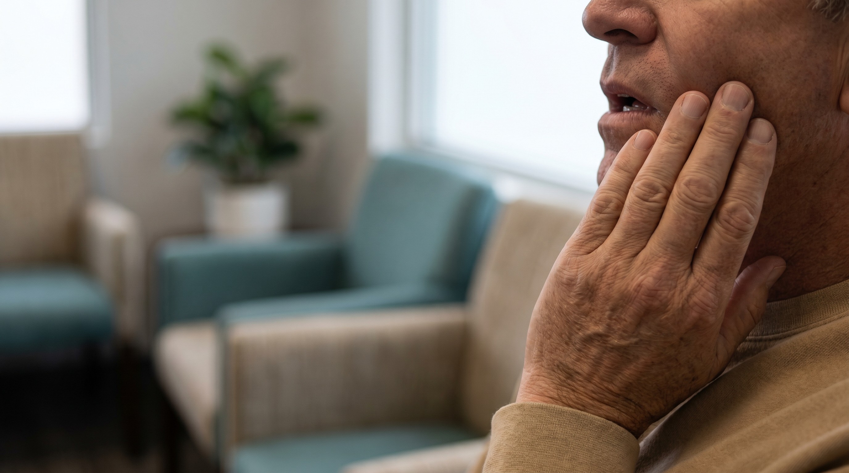 Adult patient touching cheek near jaw indicating tooth discomfort while seated indoors