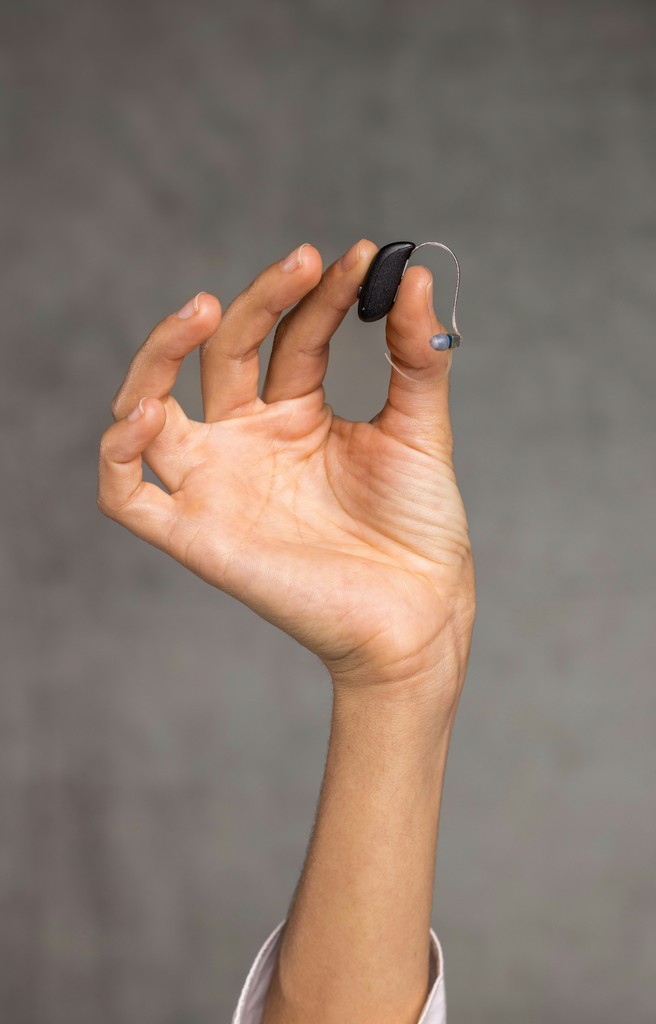 A hand is raised holding a small, dark object against a gray background.