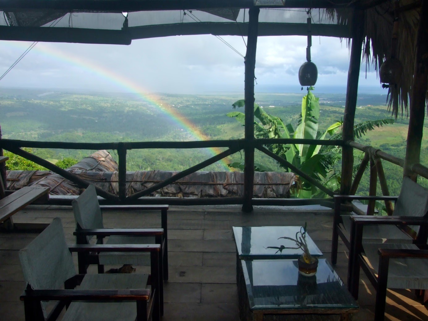 Balcony view of a green valley and a bright rainbow.