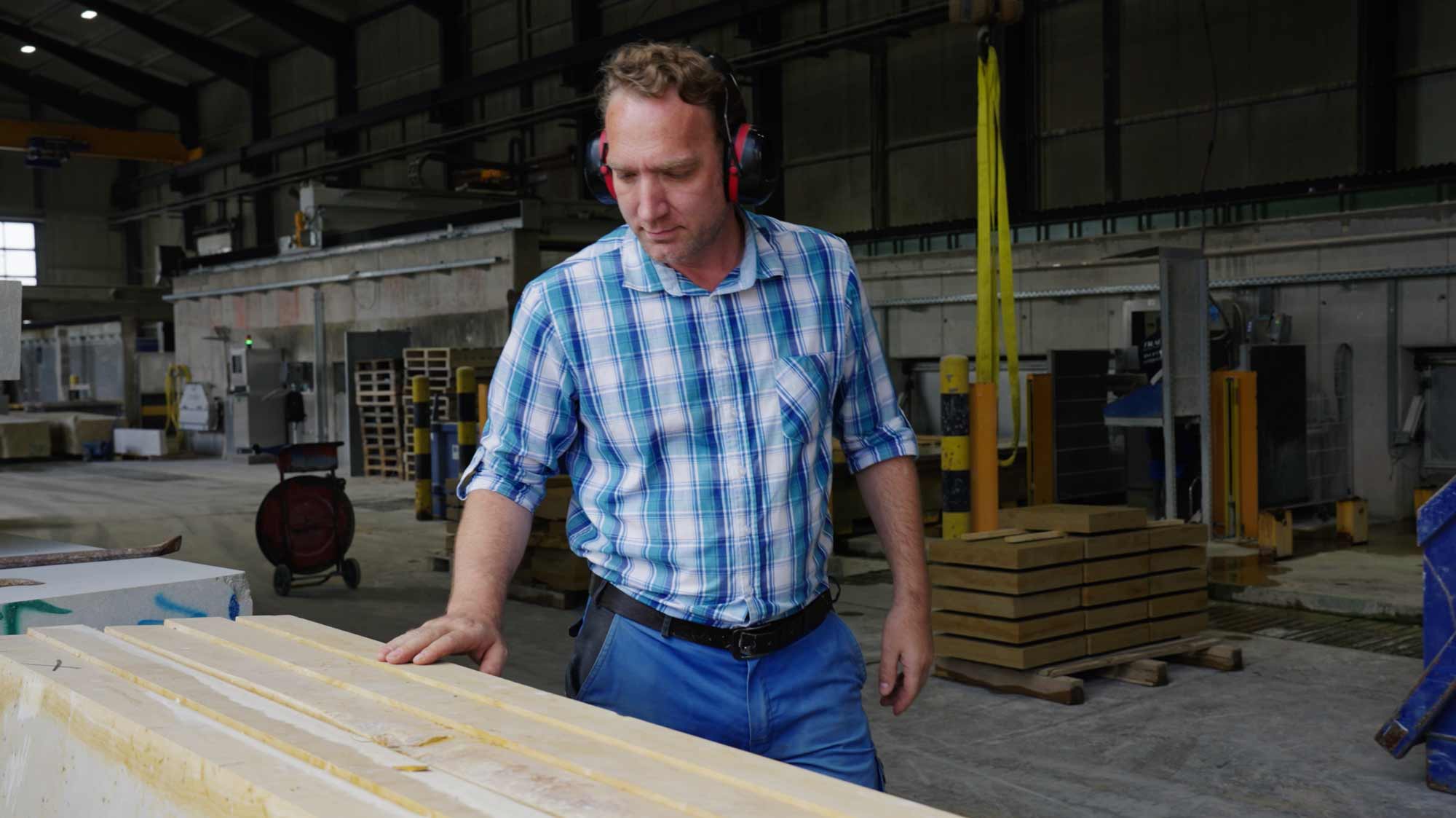 Man in a plaid shirt examines wooden planks in a factory setting, ideal for filmproduction ads and storytelling campaigns.