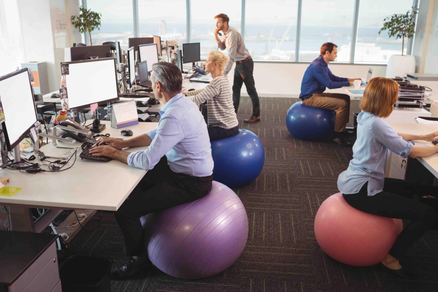 Colaboradores en oficina utilizando pelotas de ejercicio como sillas para promover bienestar laboral