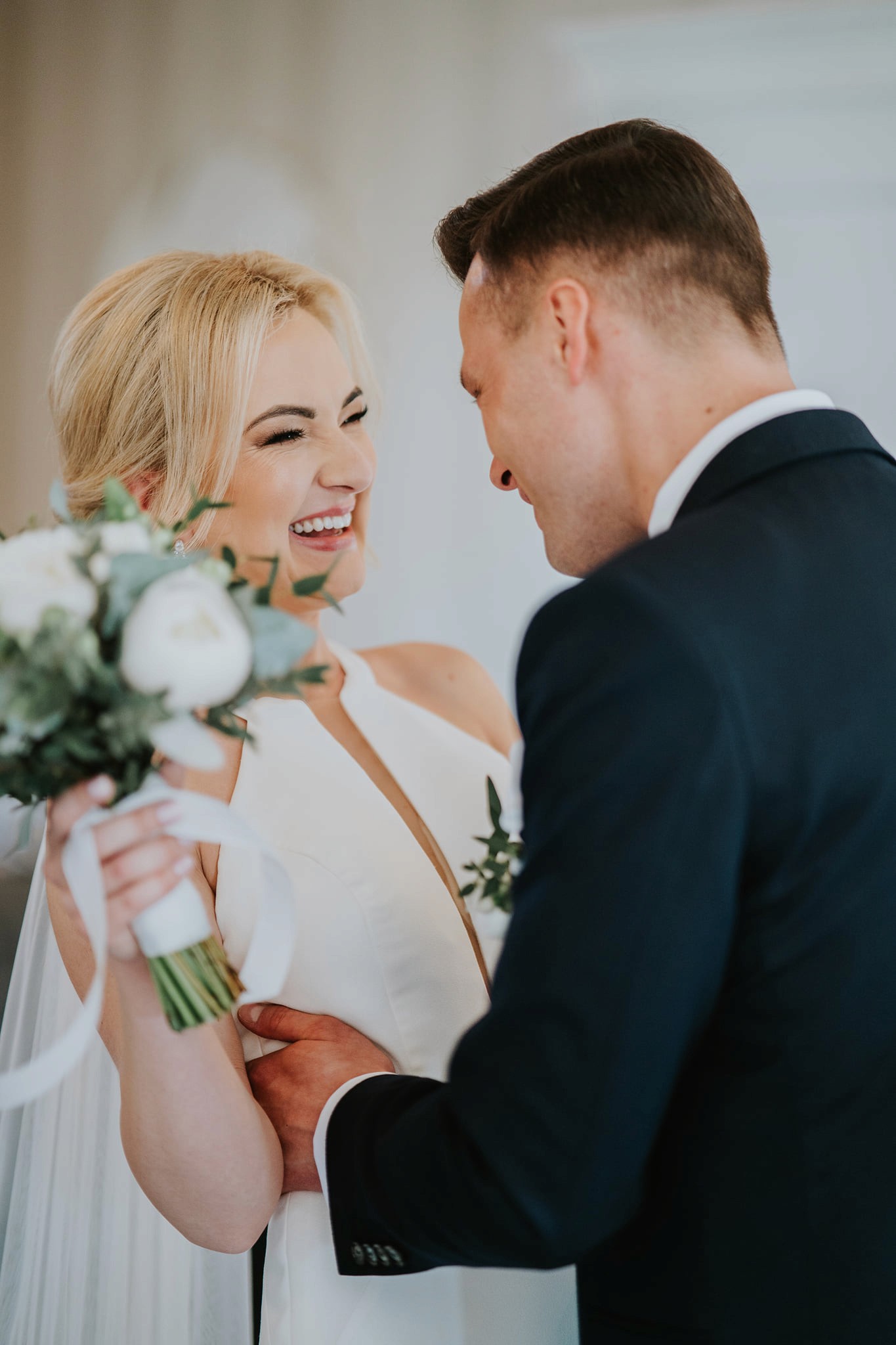 A couple in wedding attire walks hand in hand across a sunlit field.