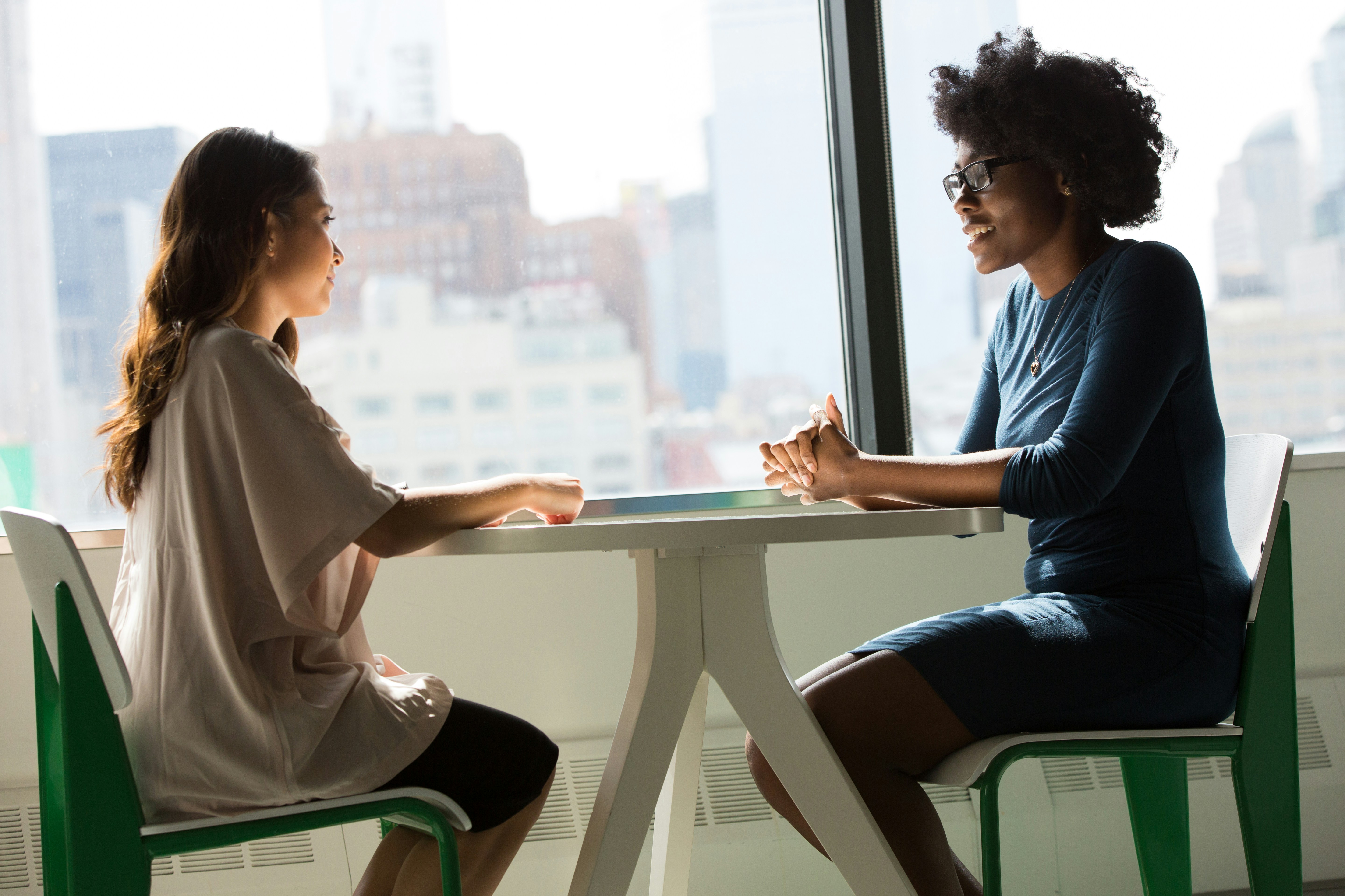 Two people sit across from each other on a table, chatting with one another.