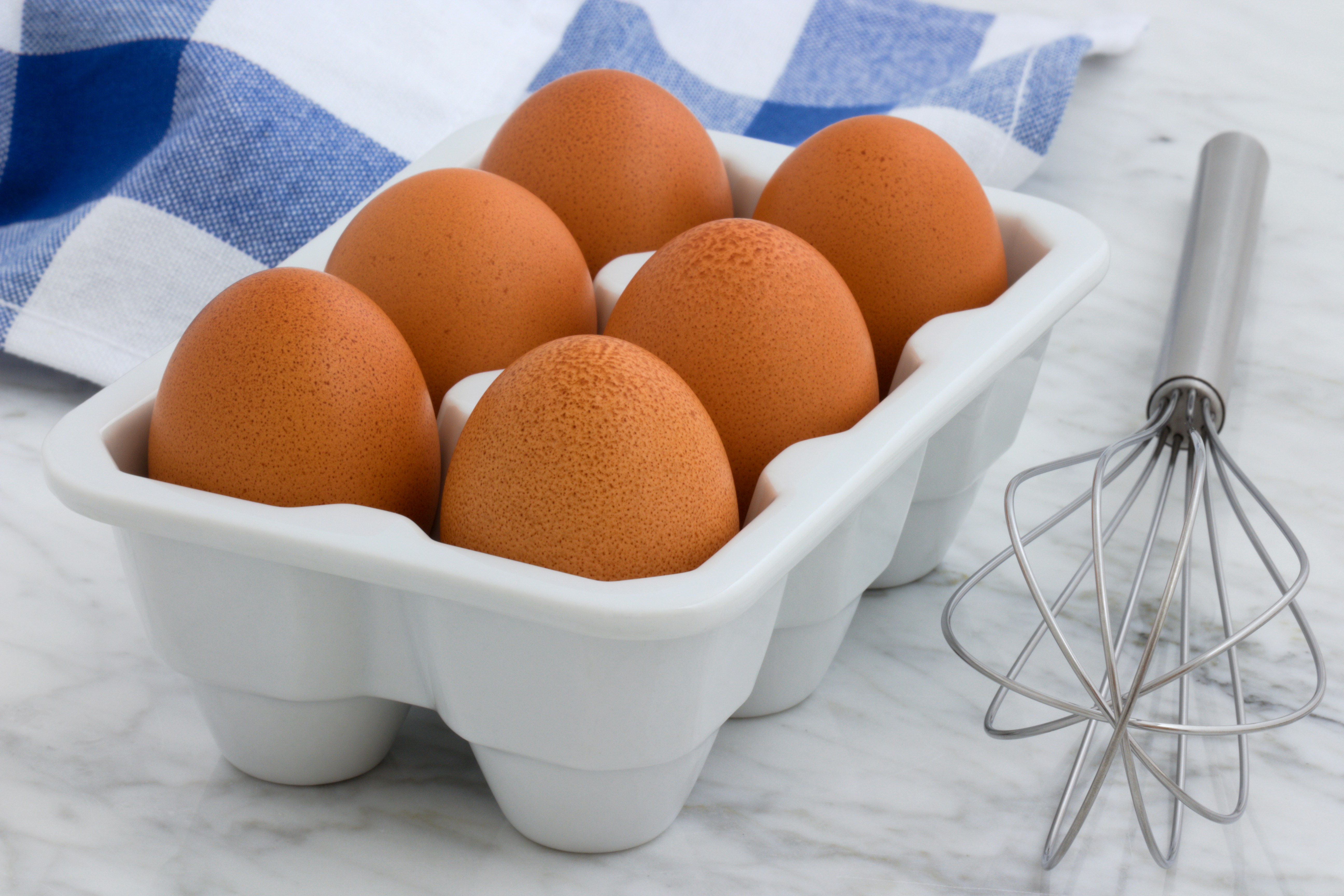 Fresh brown eggs in a carton with a whisk, showcasing the dairy and egg section at International Food Market Orlando, where you can find fresh dairy products and farm eggs.