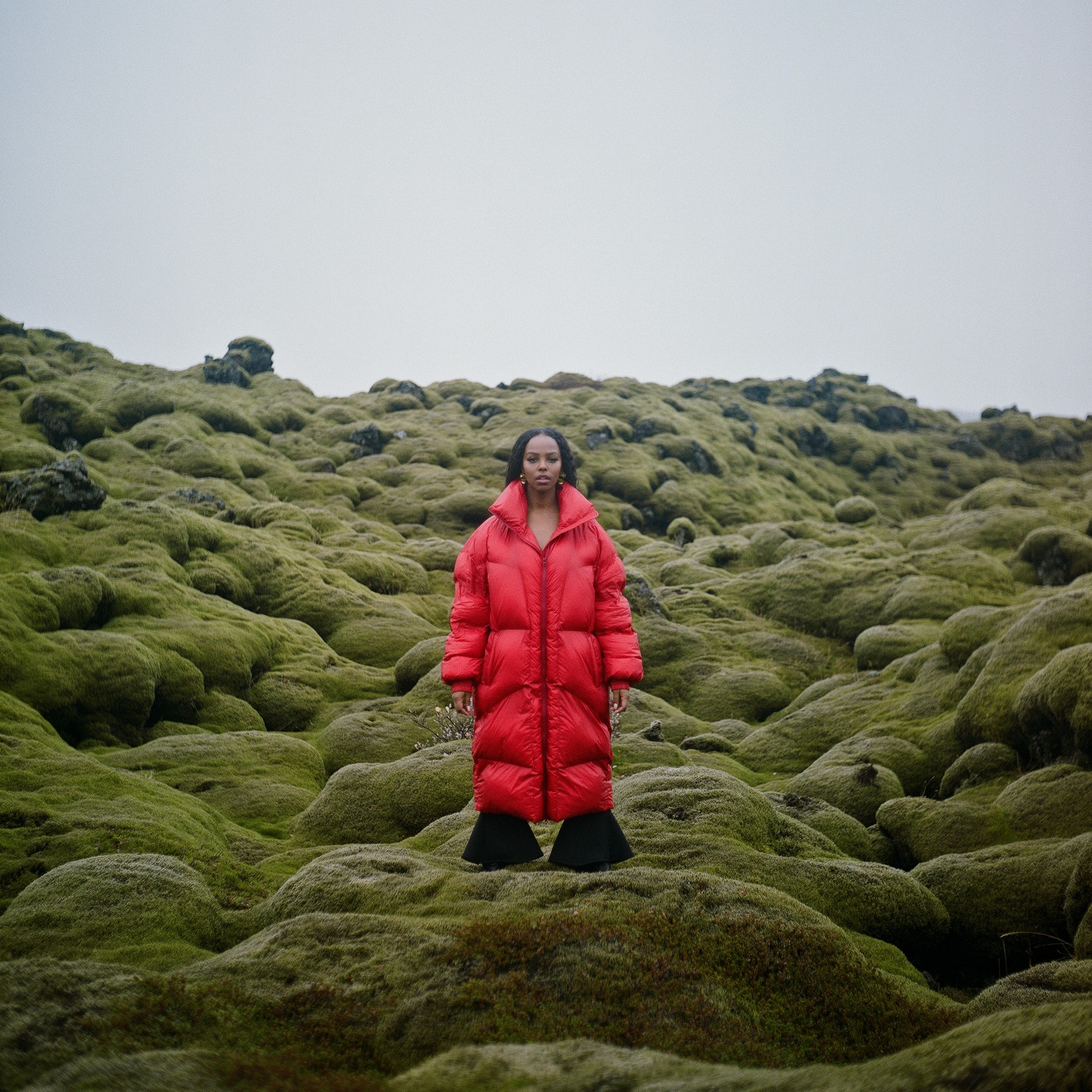 Amaal standing in a red puffer coat on a moss-covered lava field