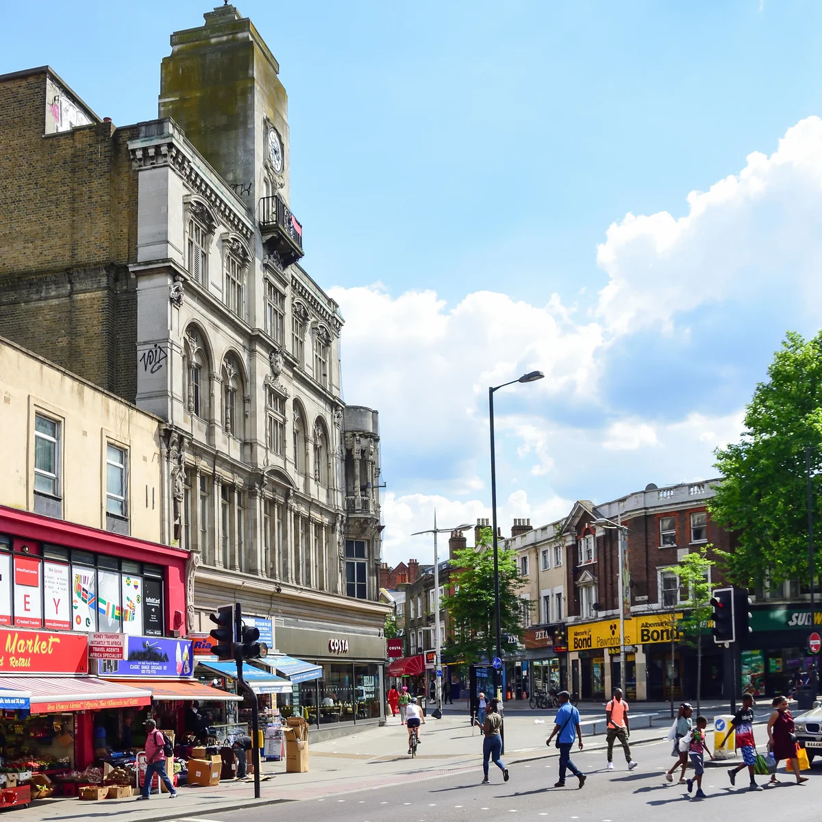 A smiling man with curly hair is sitting at a desk, looking at the camera, with a laptop and a lamp in the background.