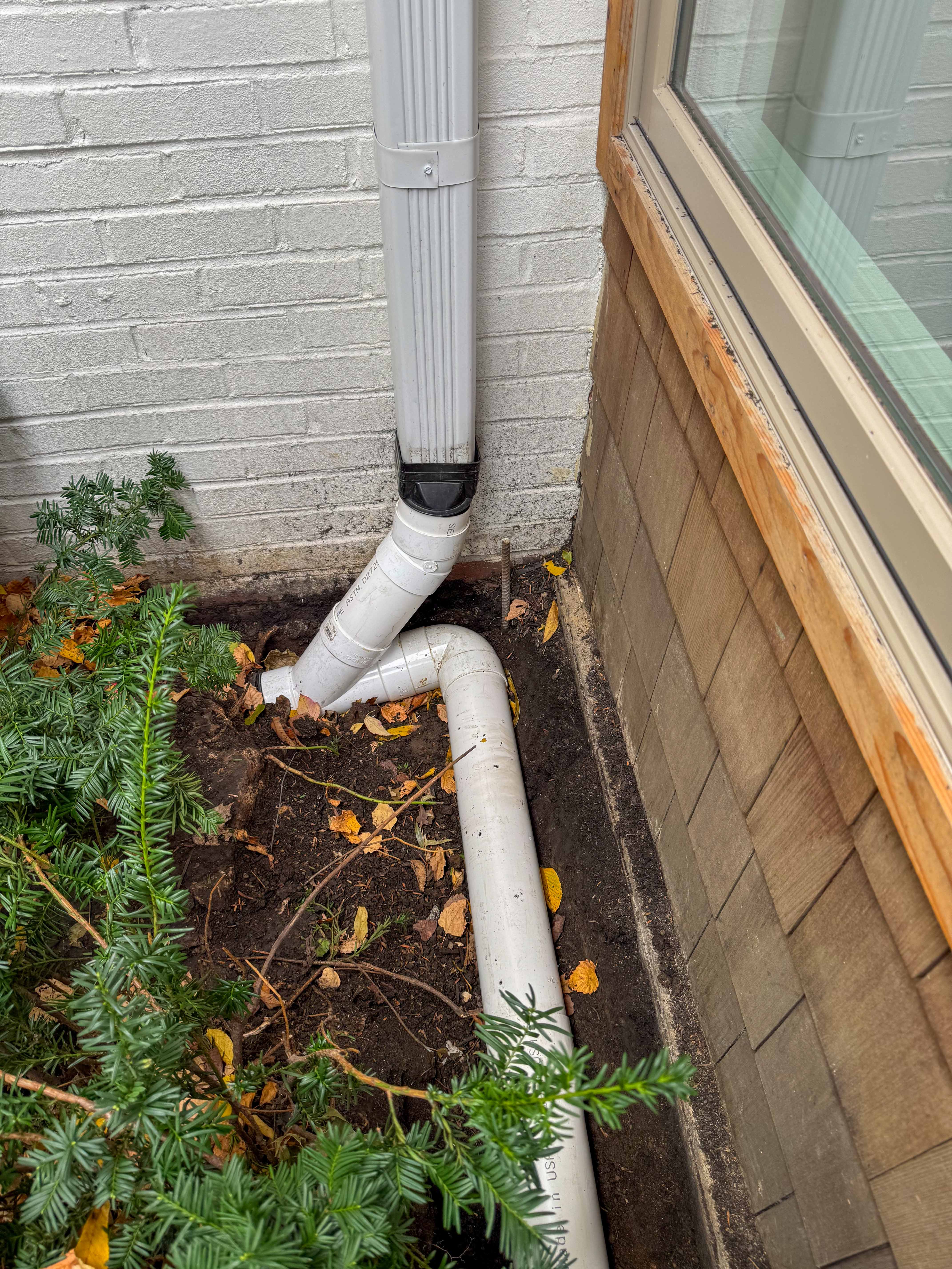 Downspout connection detail beside house foundation