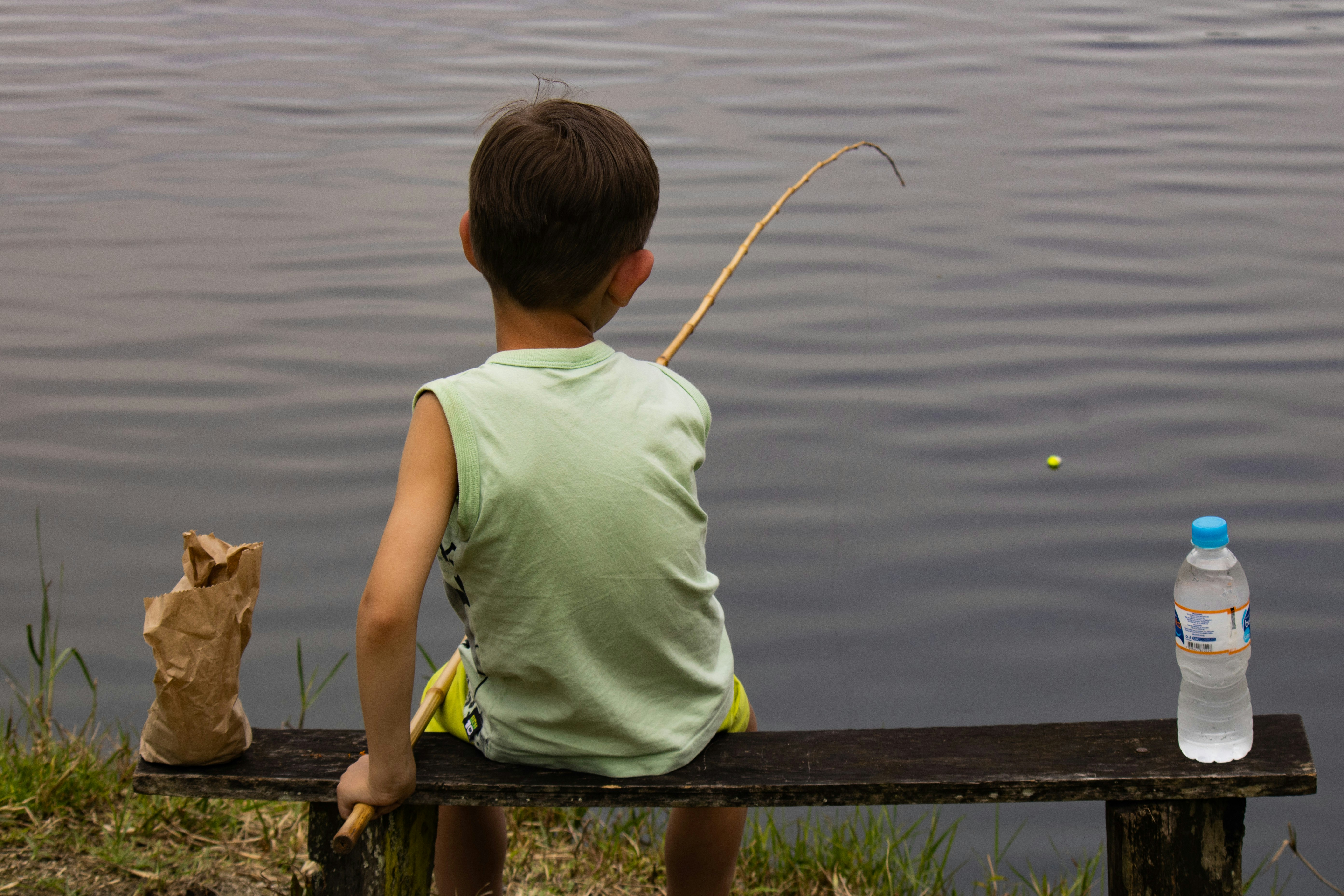 A young boy fishing from a bench by the water