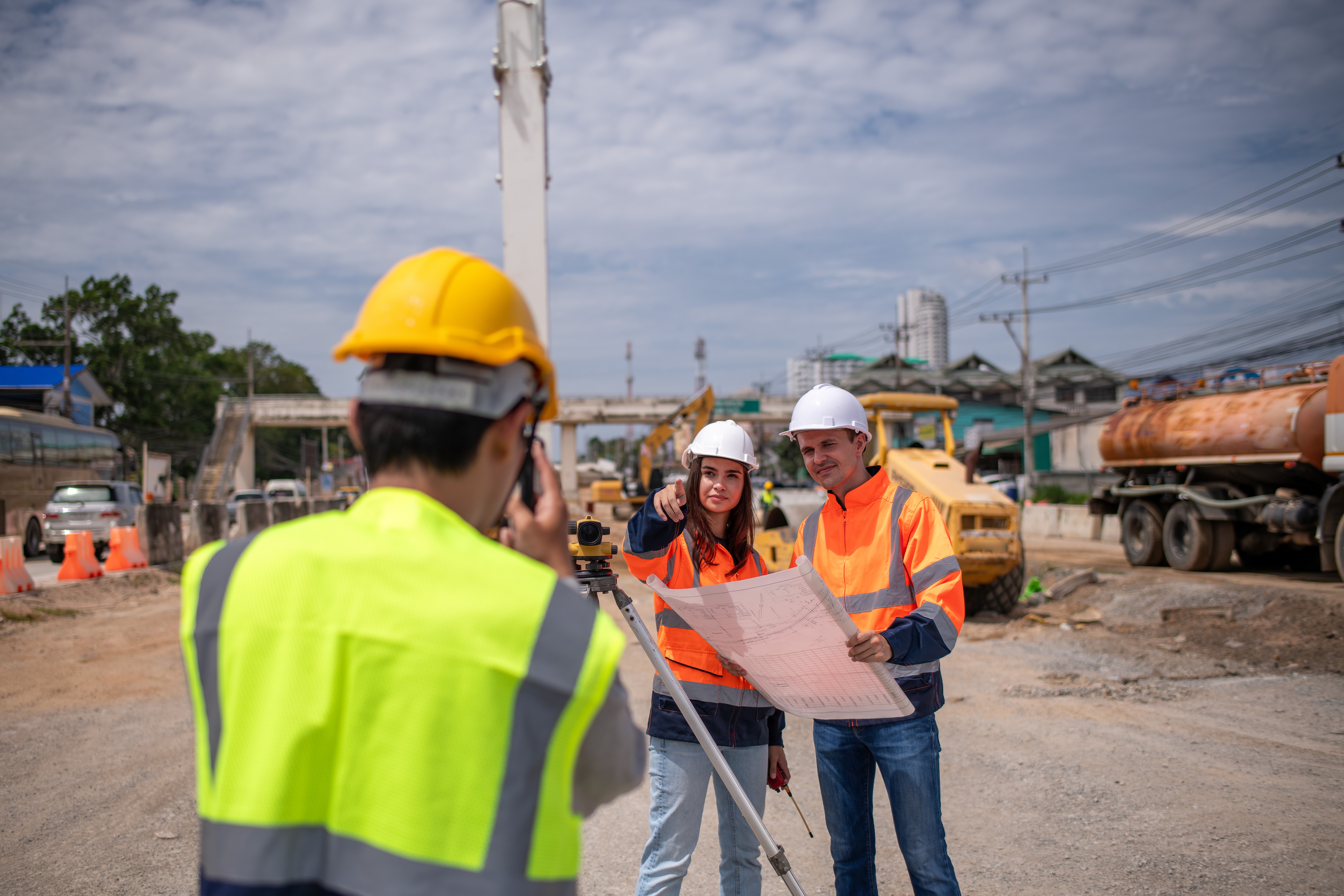 Three engineers in helmets and jackets working at a construction site.