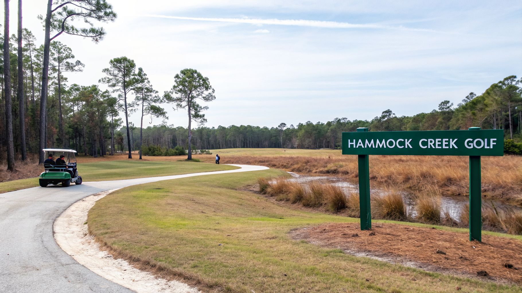 A green sign for Hammock Creek Golf on a course with a golf cart, trees, and marsh.