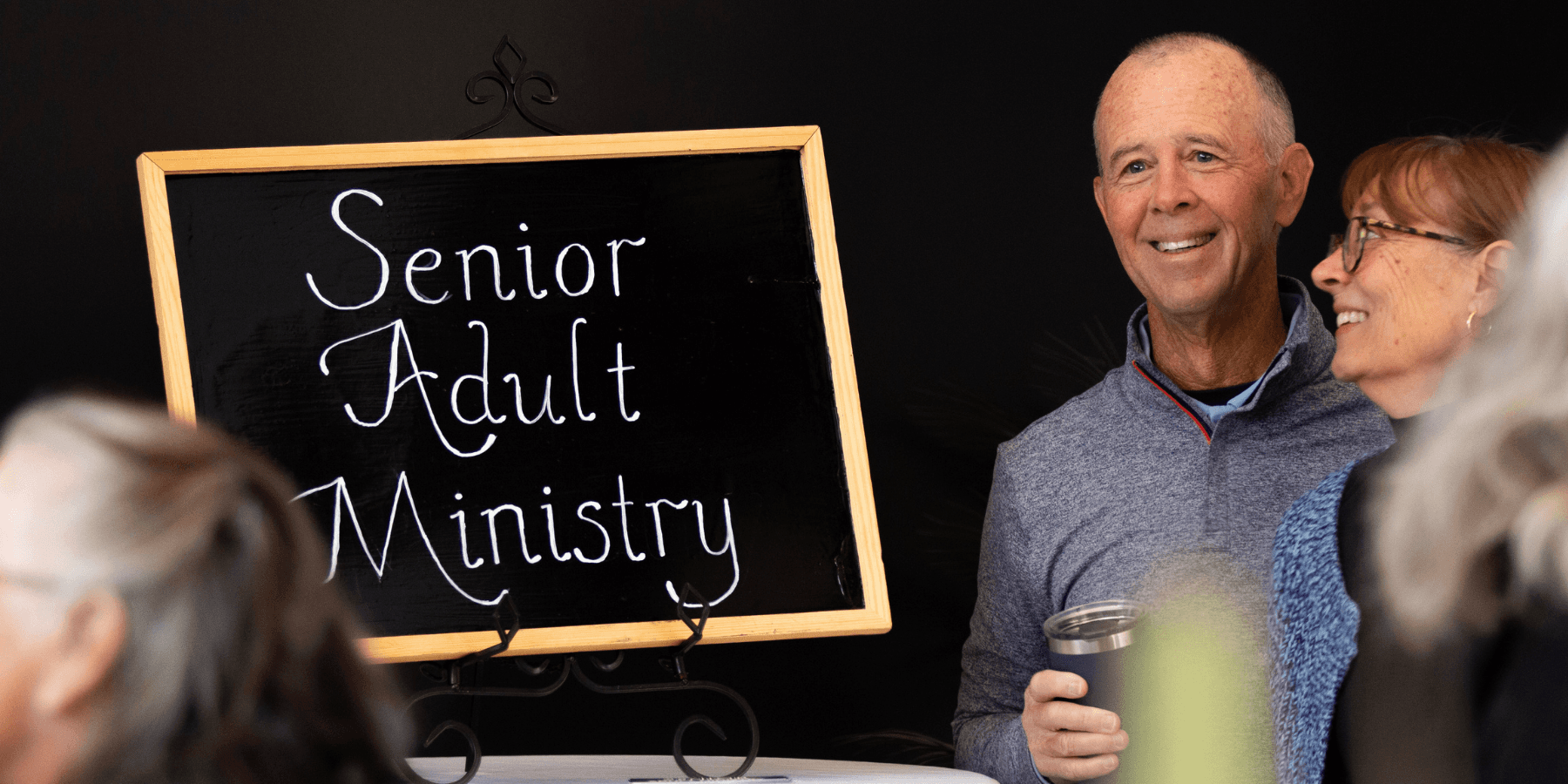 Couple smiling next to a sign that says Senior Adult Ministry