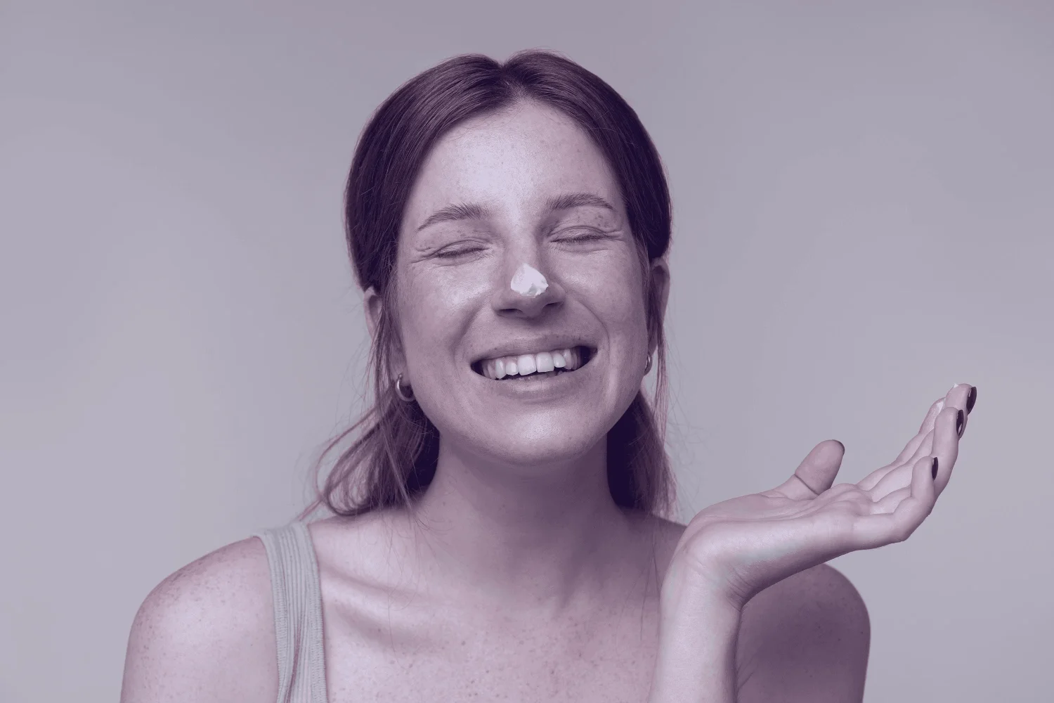 Smiling woman with a dab of moisturizer on her nose, eyes closed, enjoying her skincare routine