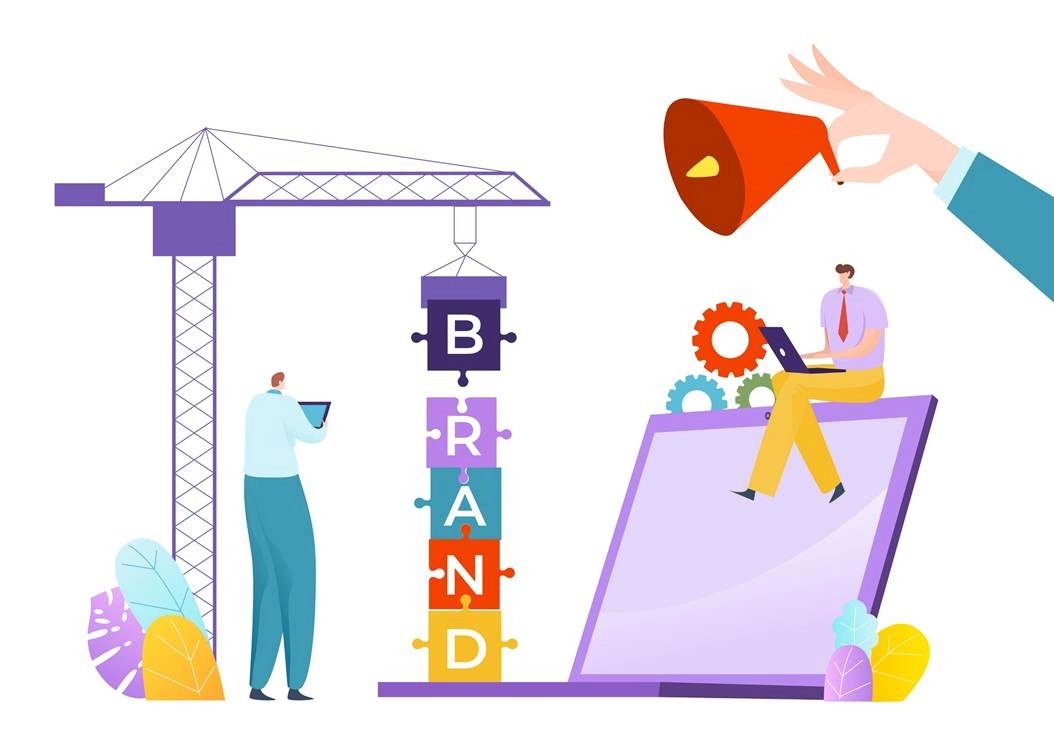 Illustration of puzzle pieces spelling BRAND being crane-lifted into place alongside a laptop, representing brand marketing strategy