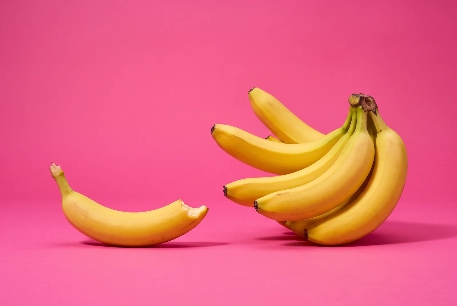 Chaser effect and priming: a single banana with one bite taken out, the rest of the bunch leaning toward it on a hot pink backdrop