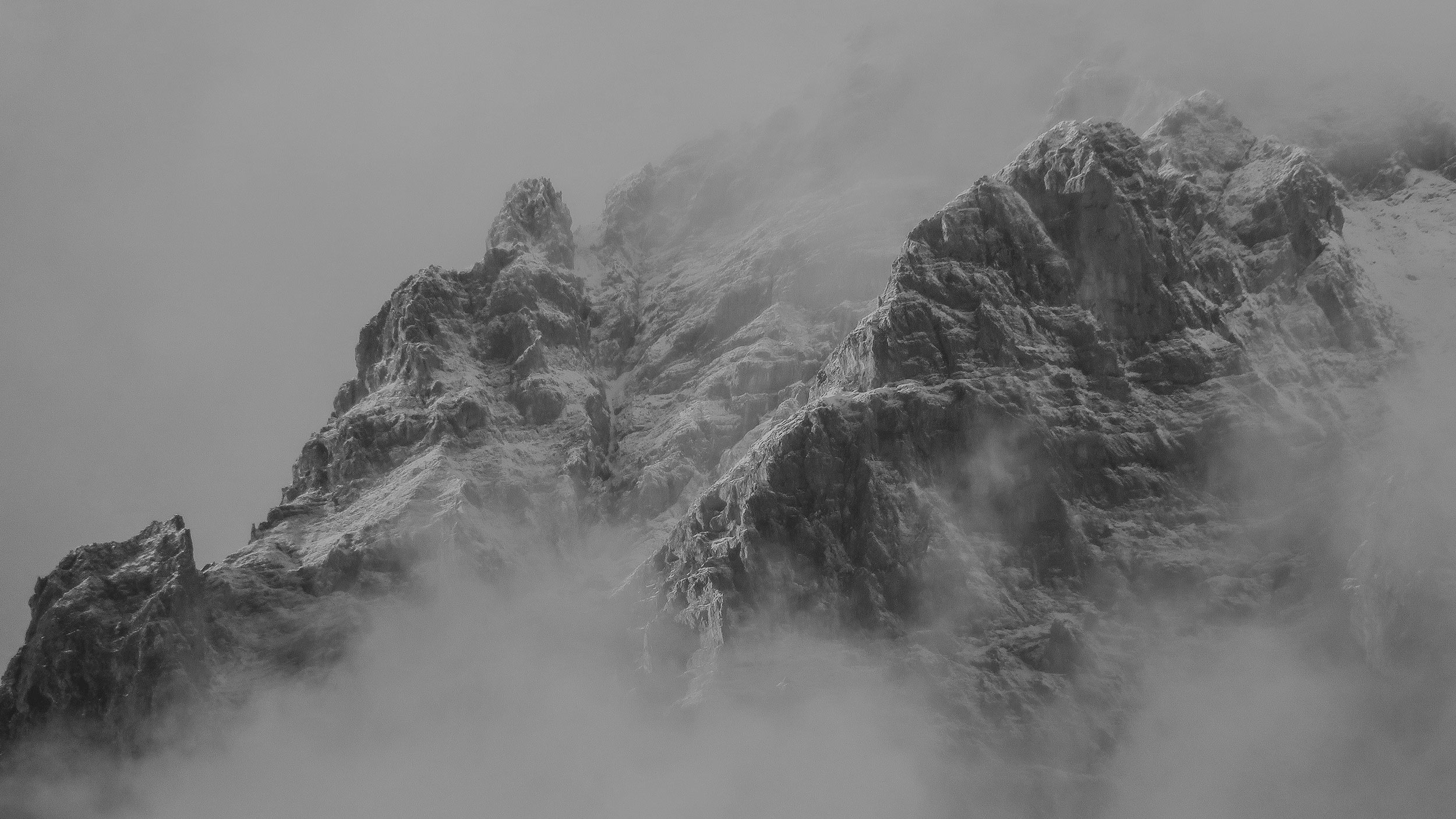 A black and white photo of a rocky mountain peak shrouded in mist and clouds.