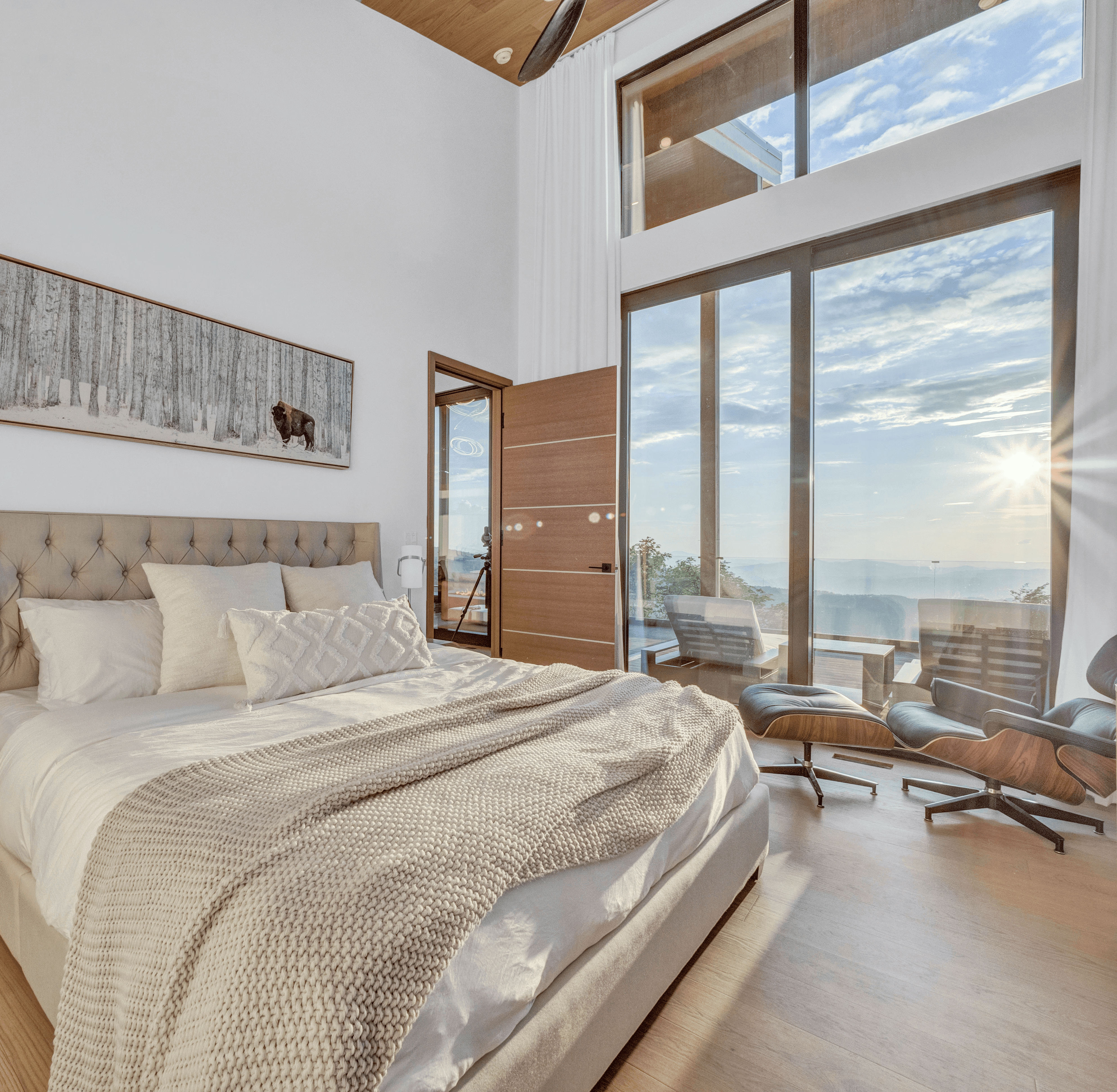 Expansive master bedroom at golden hour with a sunburst effect through floor-to-ceiling windows and a view of the mountains