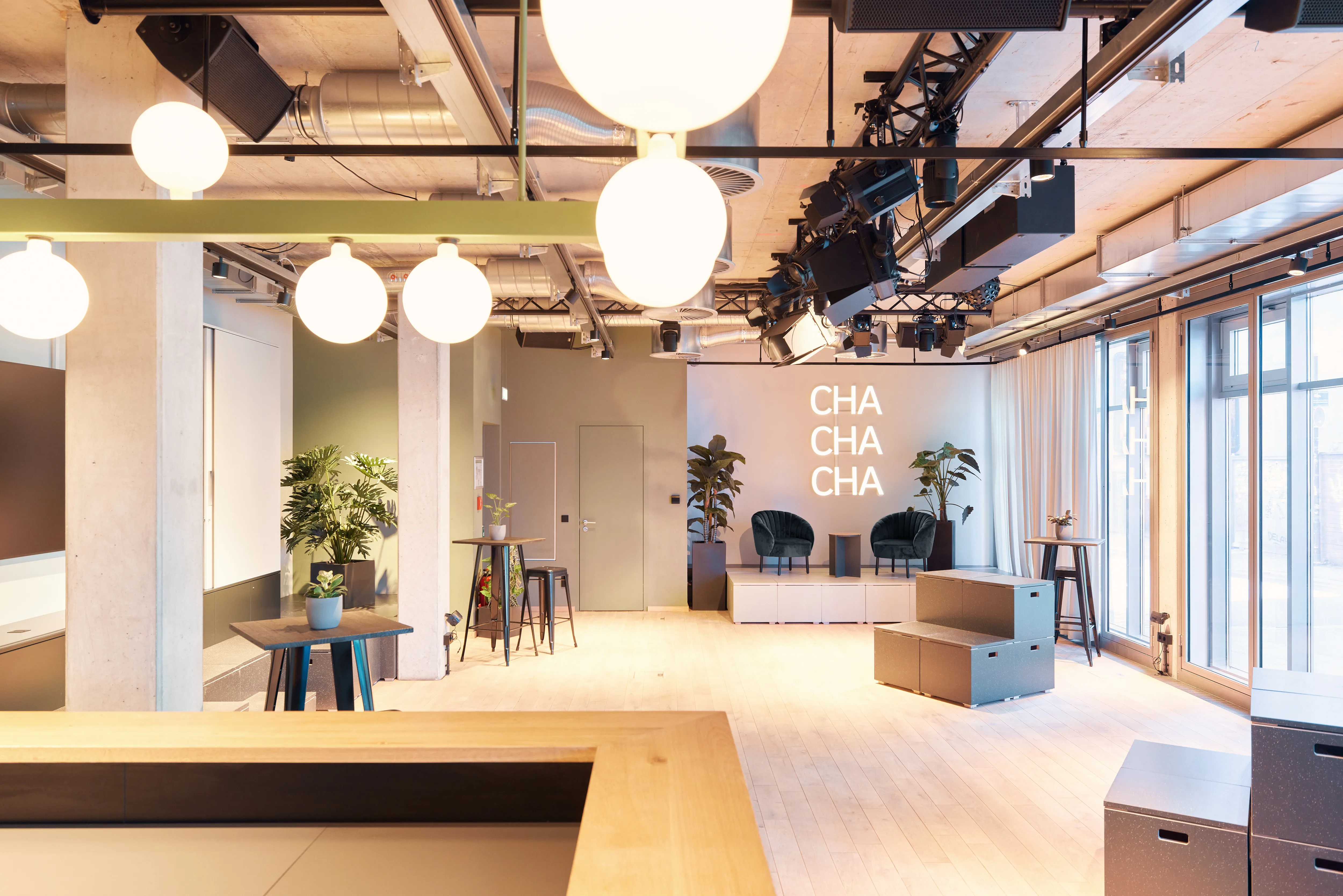 Overview of 381 EVENT SPACE with white globe pendant lights, wooden counter, high tables with blue stools, grey seating cubes and a CHA CHA CHA lettering wall.