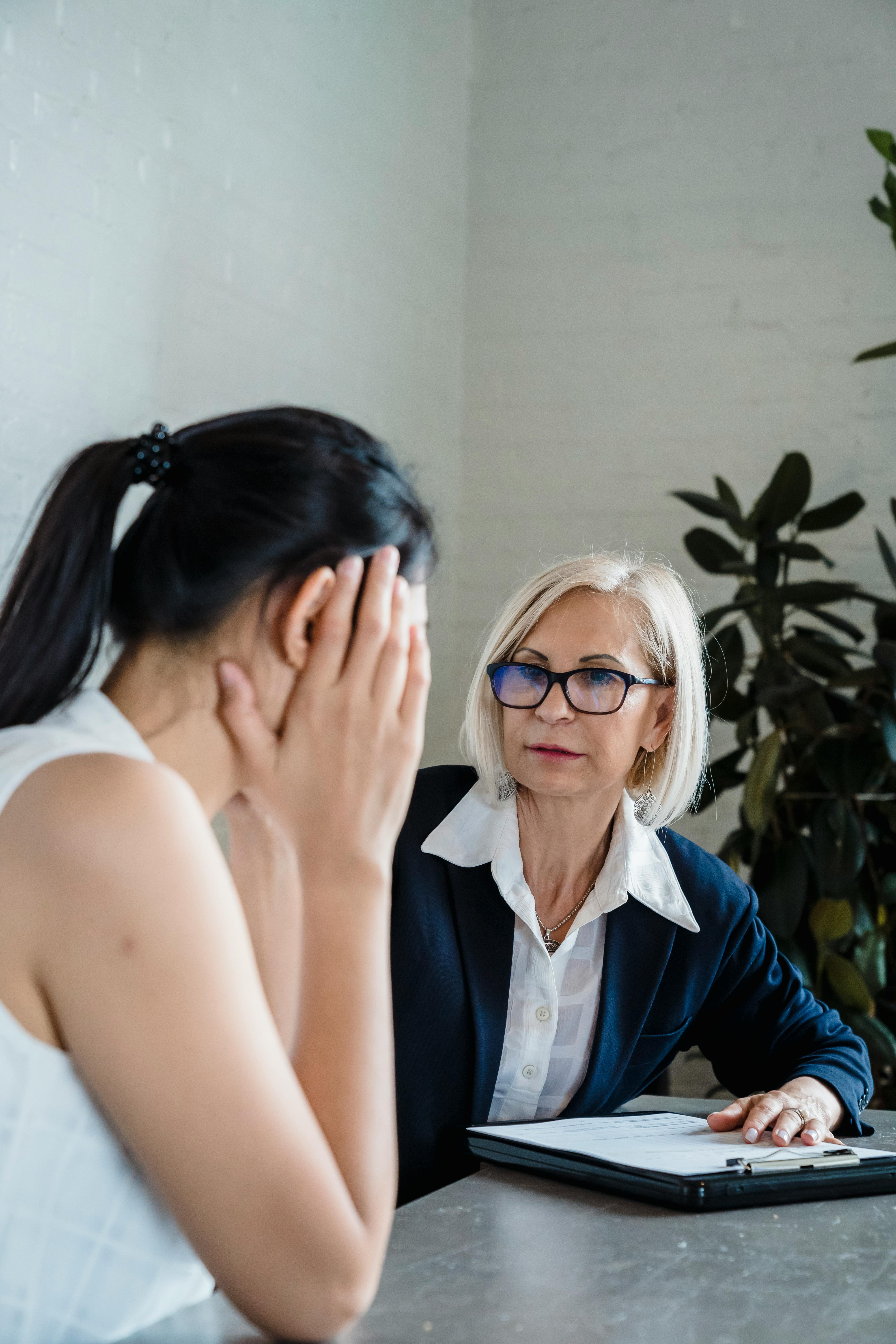 Donna anziana con occhiali che ascolta attentamente una giovane donna durante un colloquio, rappresentazione di supporto, ascolto e relazione professionale.