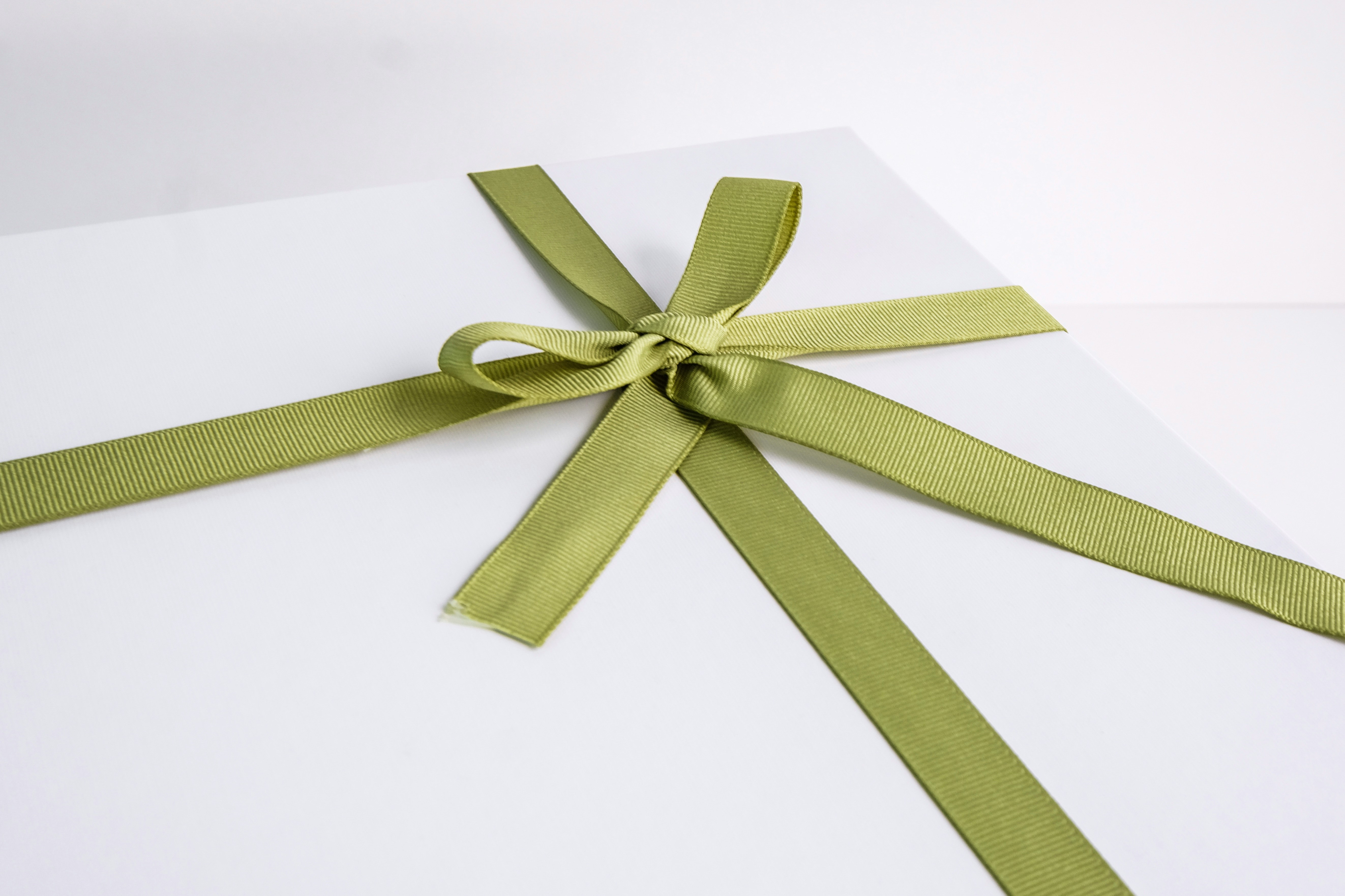 Clean white gift box tied with a green grosgrain ribbon bow