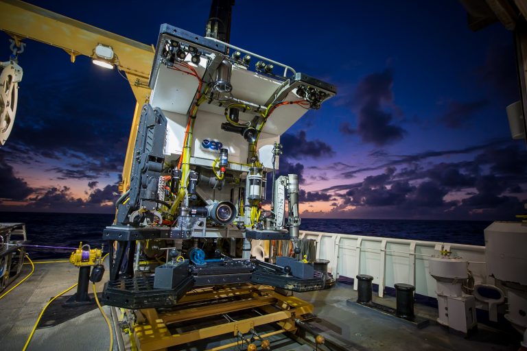 Deep Discoverer ROV with cameras, lights and manipulator arms on the deck of a research vessel at dusk