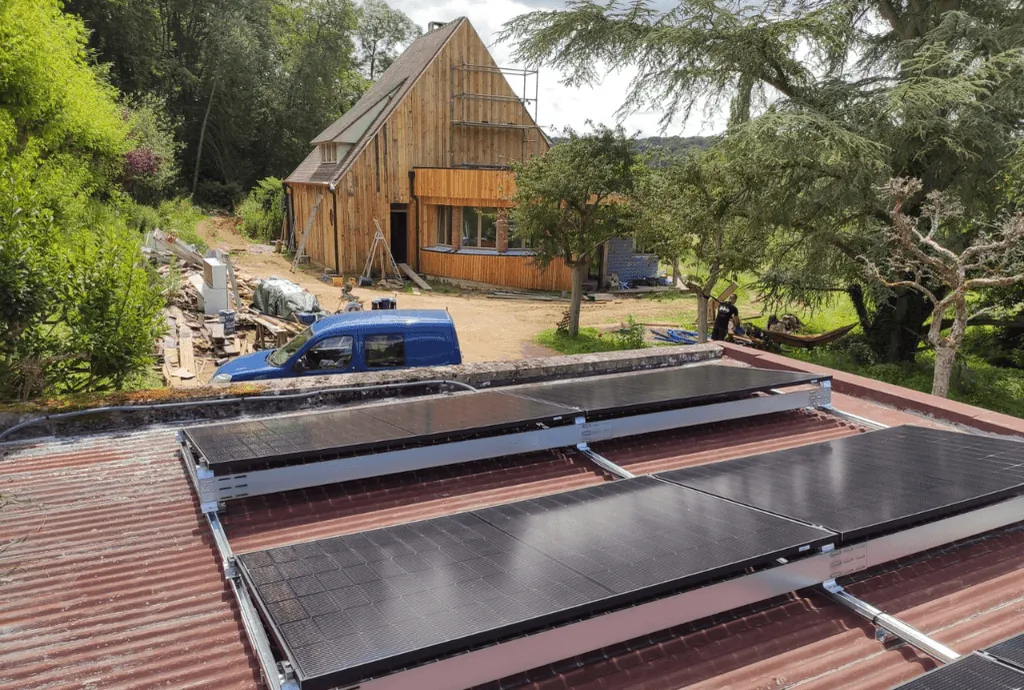 Photo de panneaux solaires qui ont été installés sur le toit d'une dépendence. On voit une maison en construction en arrière plan.