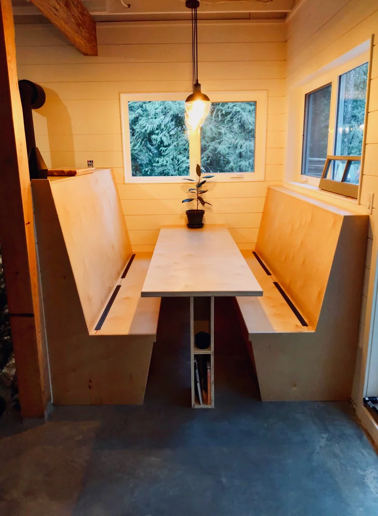 Modern two-story home with large glass windows, warmly lit interiors, and a balcony. Surrounded by trees and a manicured lawn at dusk. Cozy ambiance.