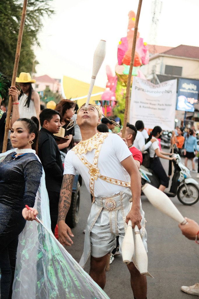 A street performer balances a juggling club on his nose during a lively festival parade, surrounded by other participants in colorful costumes and a festive atmosphere. The event showcases the vibrant cultural celebrations and street entertainment.