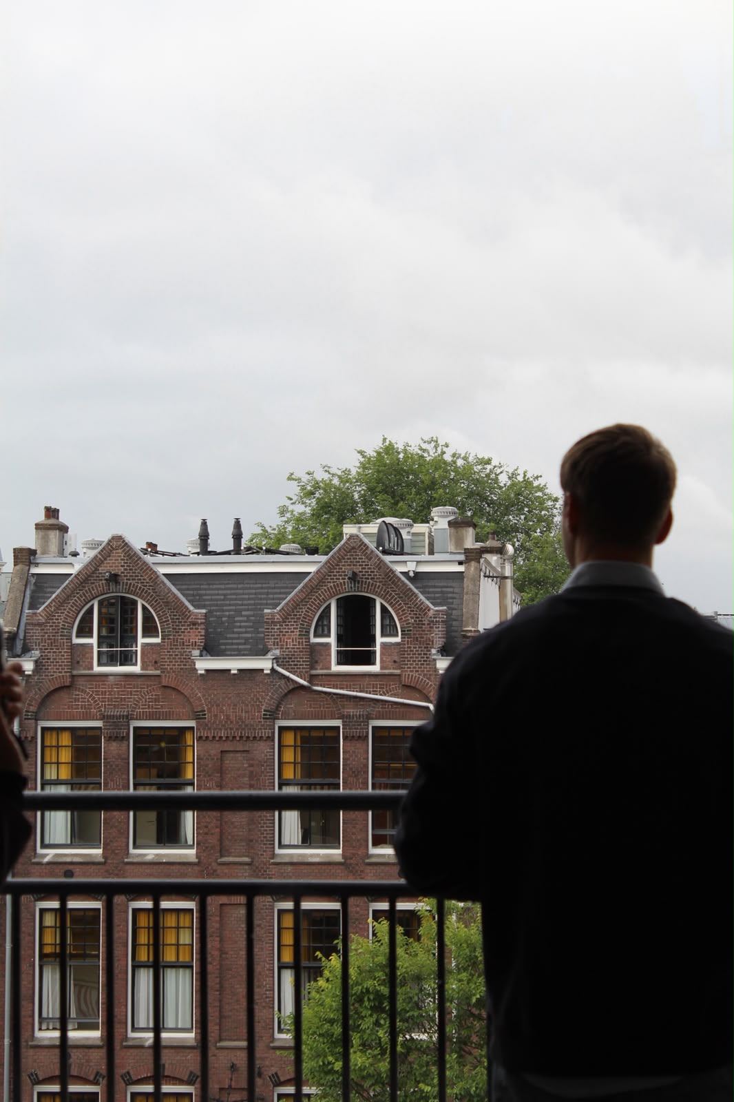 Silhouet van een professional op een balkon met uitzicht op Amsterdamse grachtenpanden
