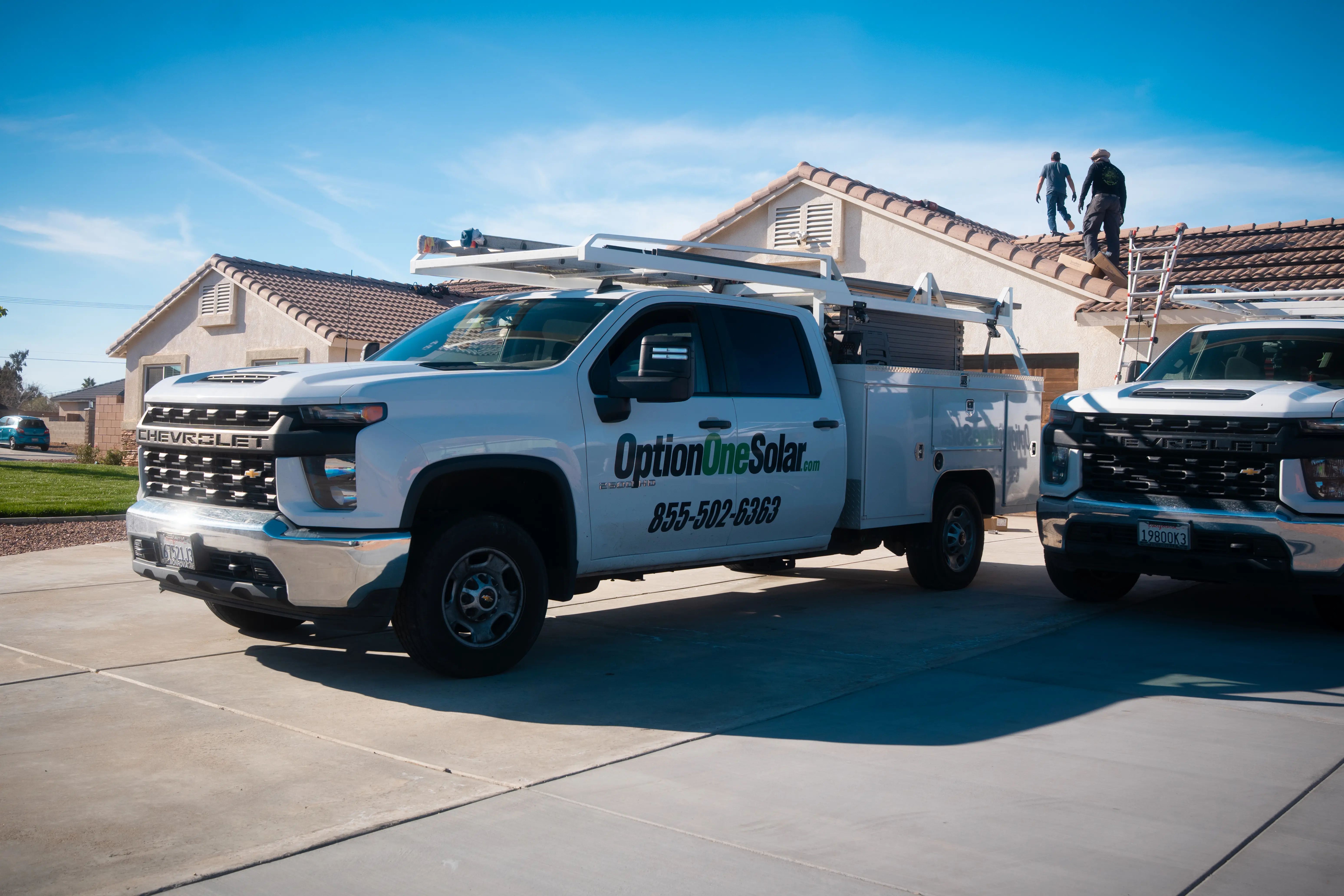 An Option One Solar service truck parked in a driveway while two crew members work on the tile roof above