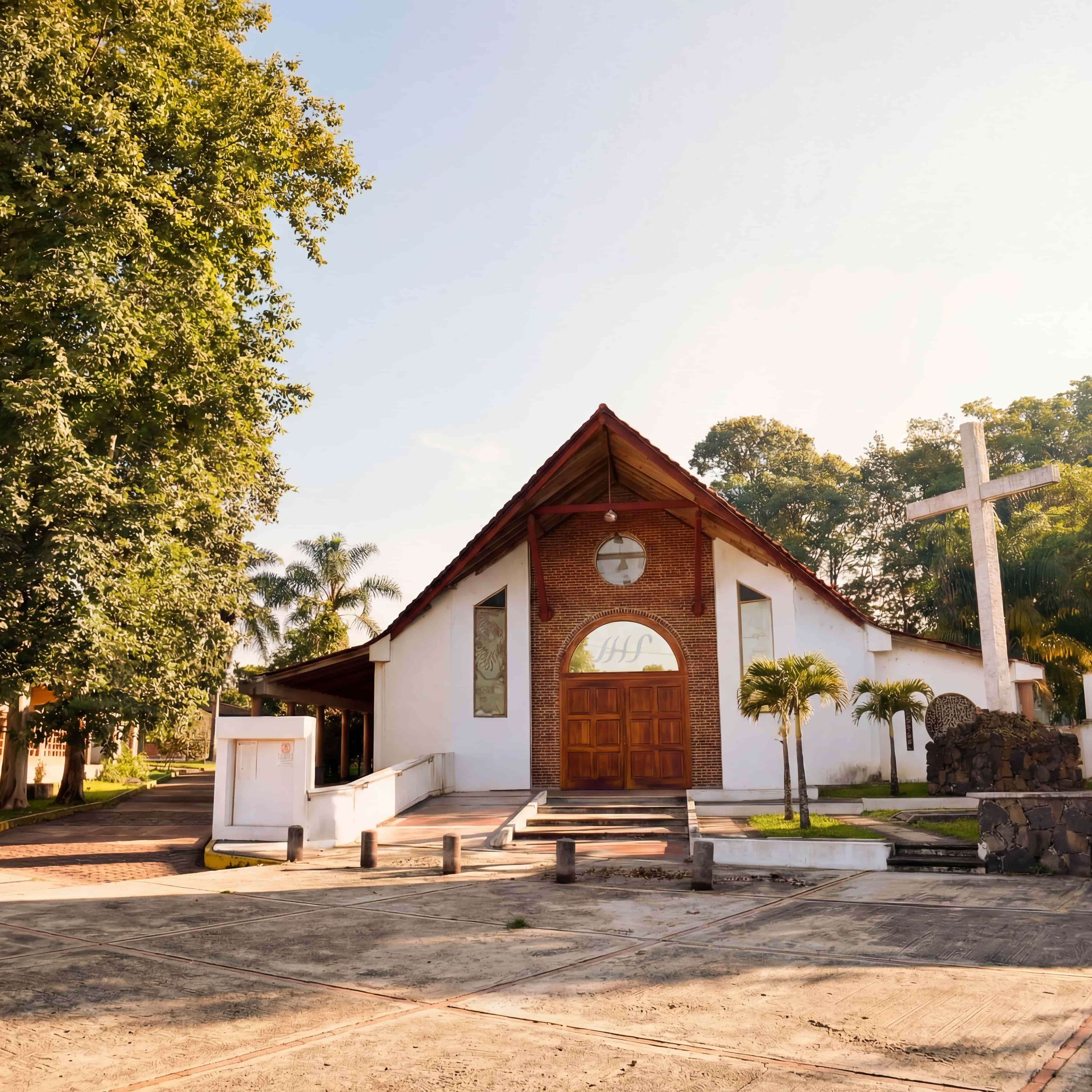 A serene outdoor wedding setup with white chairs arranged on green grass under a canopy of trees.