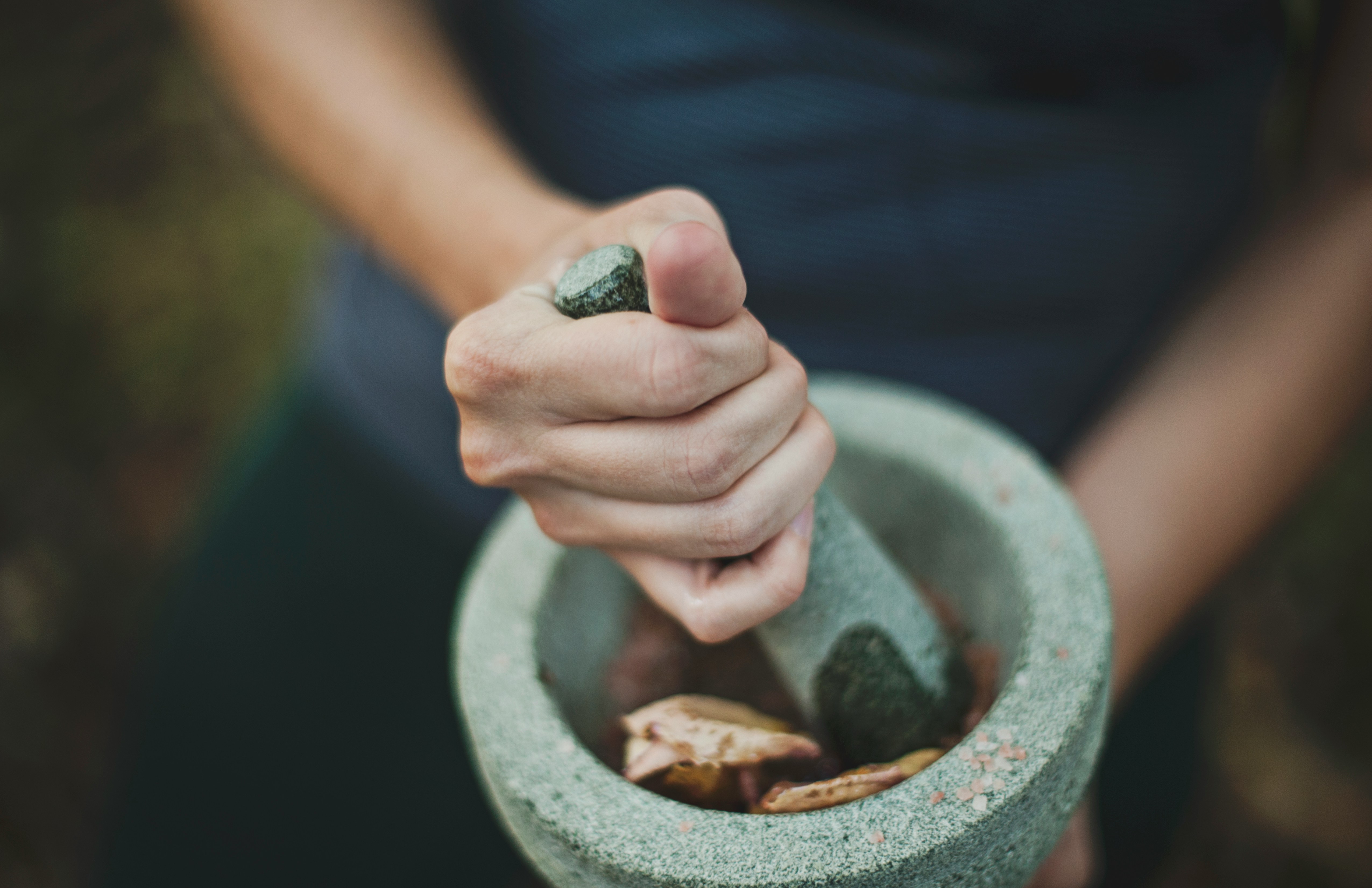 Hands grinding dried herbs in a stone mortar