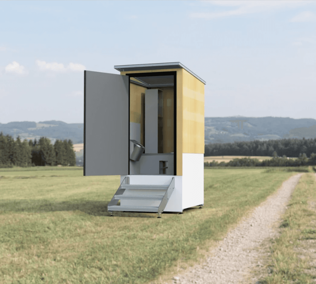 Dréchen Toilette vun NoWaSan op enger gréng Wiss, déi kee Waasser benotzt – eng nohalteg, ëmweltfrëndlech Sanitärléisung fir natierlech Landschaften.